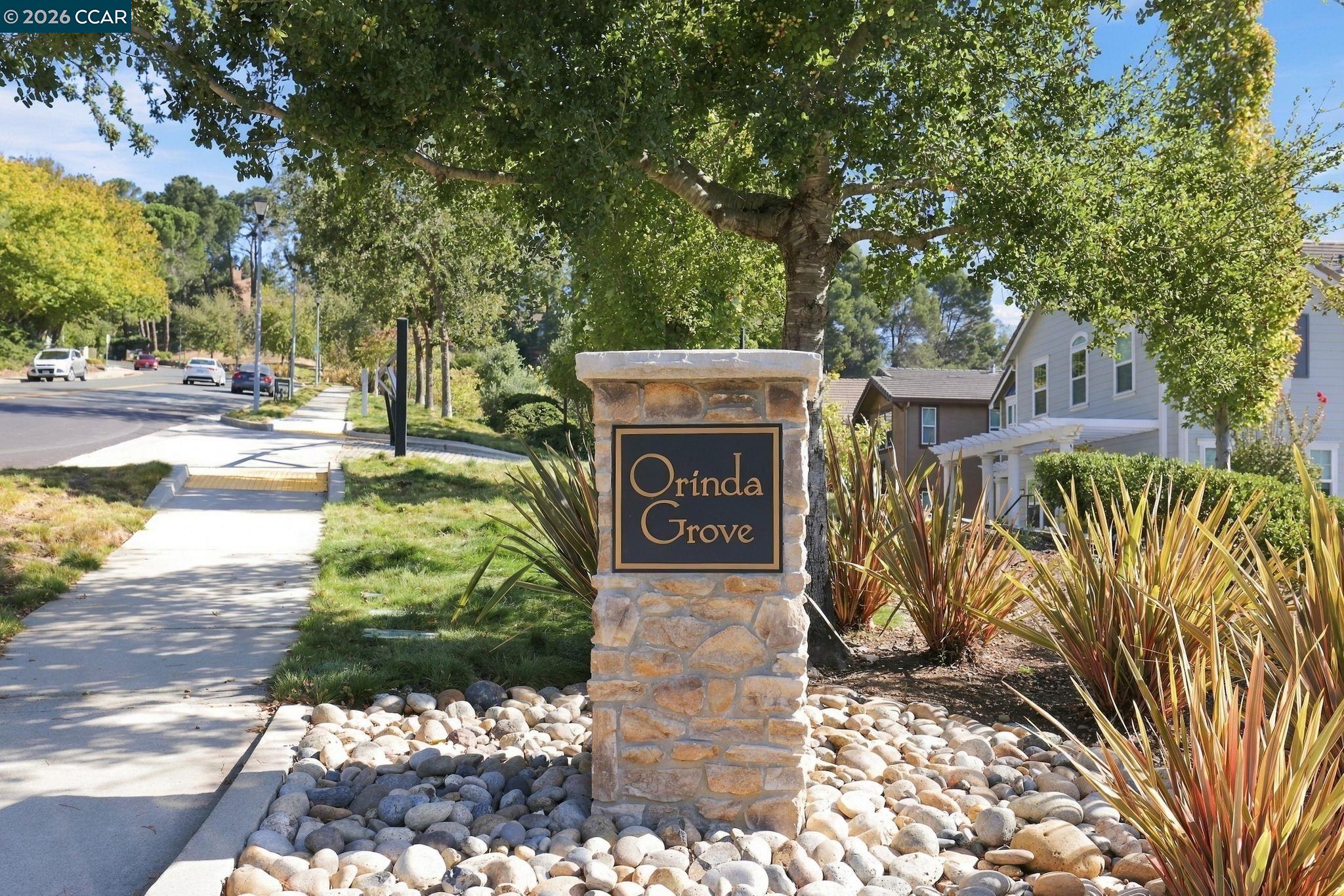 Stone Orinda Grove neighborhood sign beside a landscaped sidewalk and nearby homes.