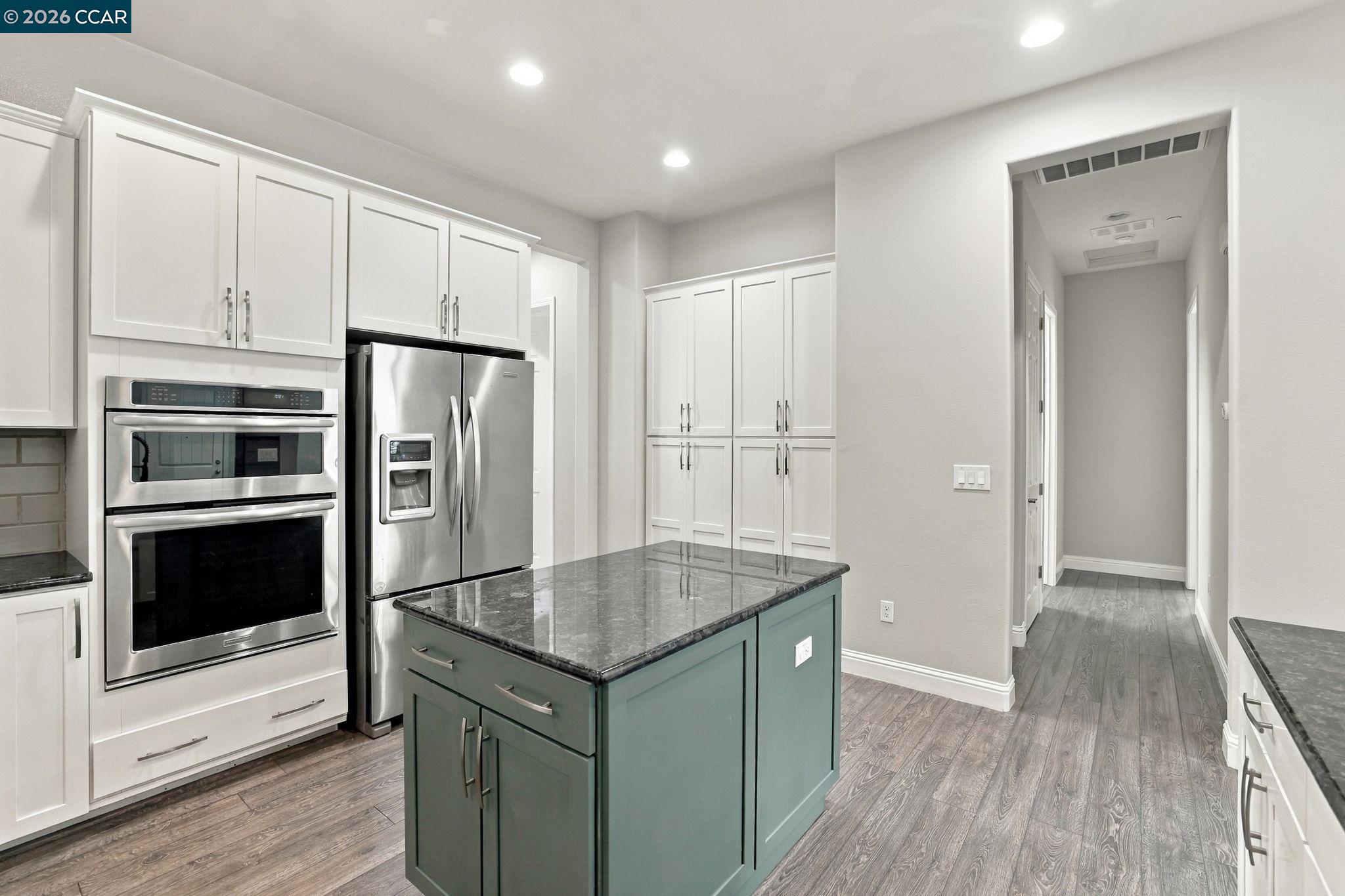 Modern kitchen with stainless steel appliances and a dark stone-topped teal island.