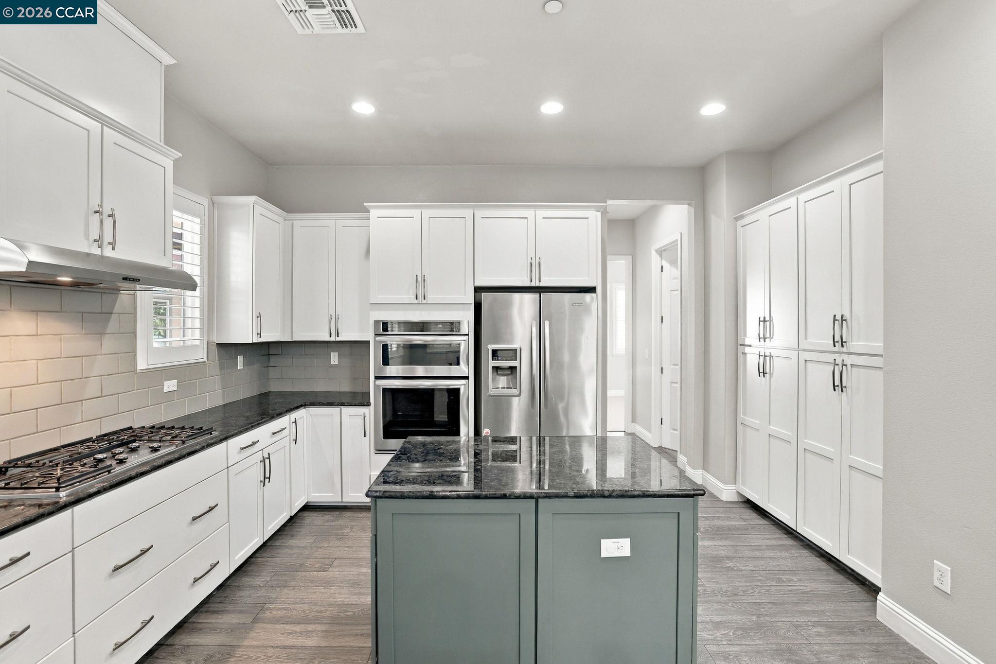 Kitchen with a gray-green island, dark stone counters, white cabinetry, and stainless-steel appliances.
