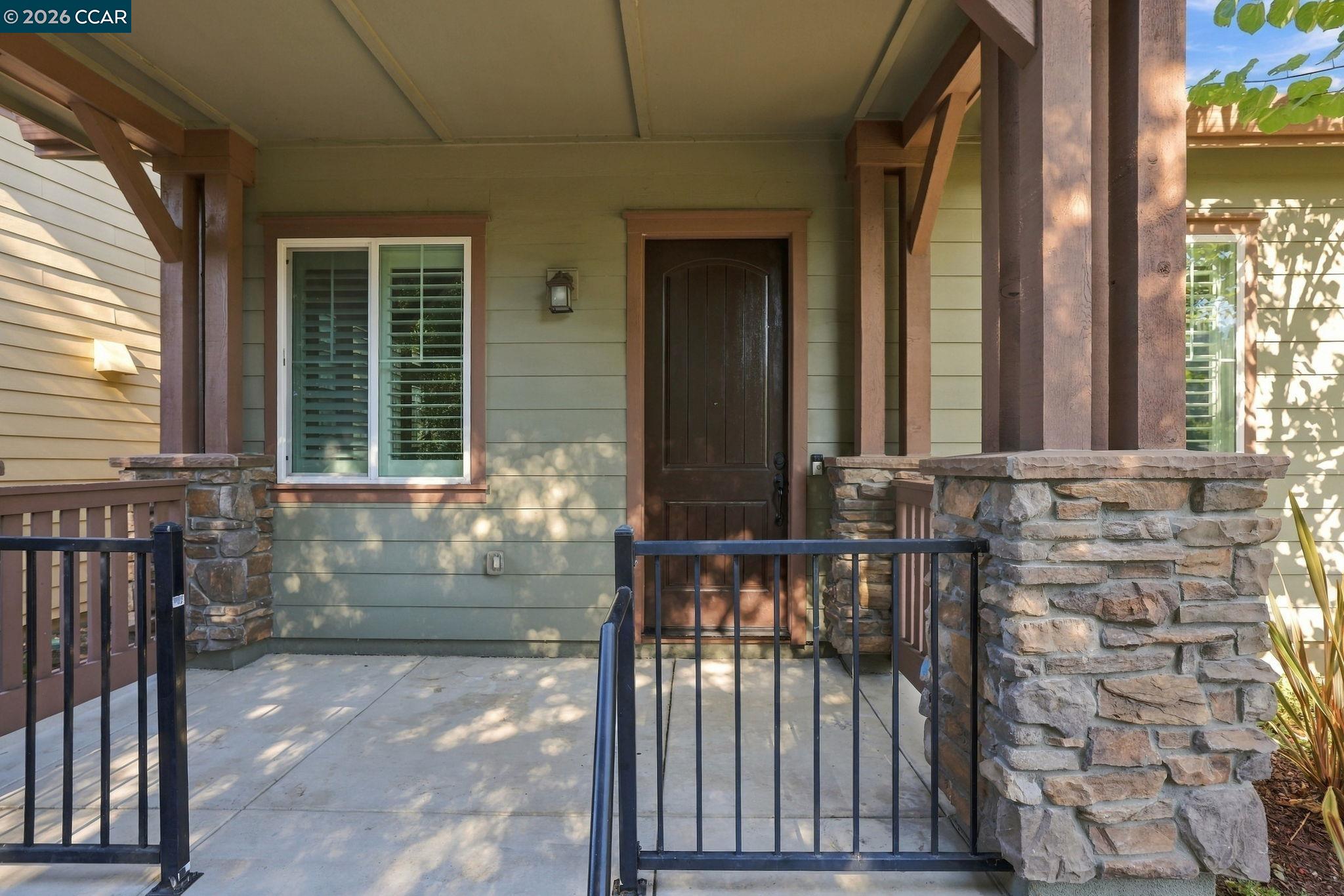 Covered front porch with a dark wood door, stone pillars, and black metal railings.