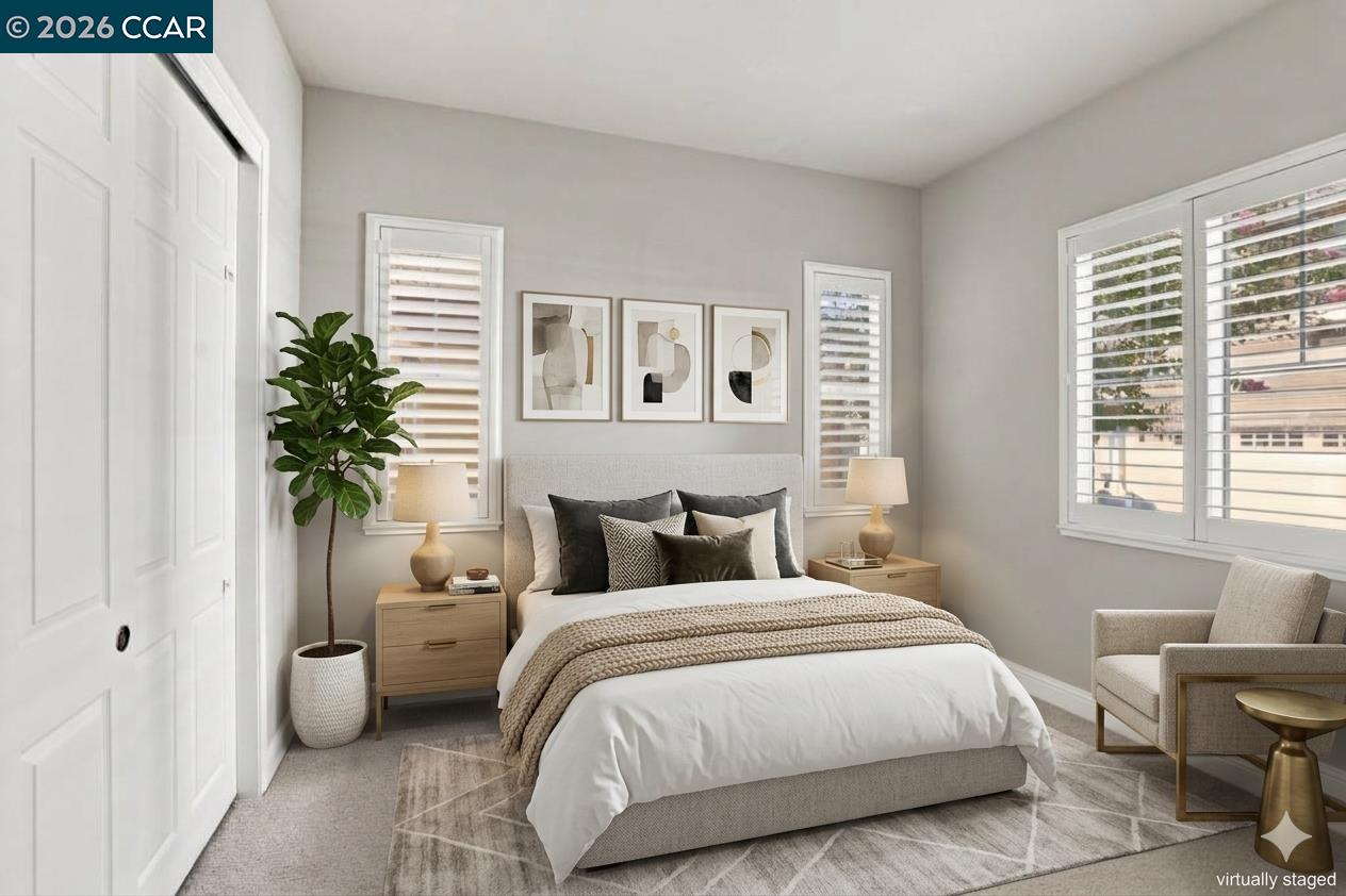 Staged bedroom with a white bed, neutral bedding, framed art, and shuttered windows.