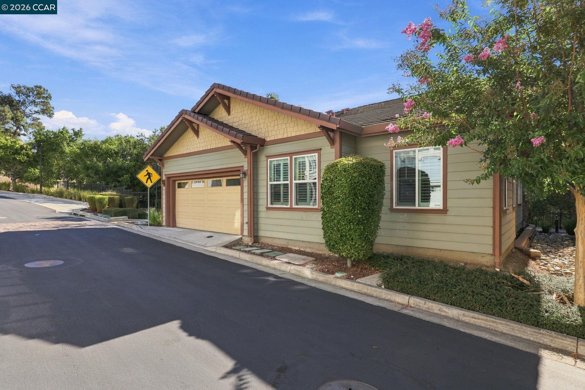 Single-story home with a garage, green siding, and pink flowering trees along the street.