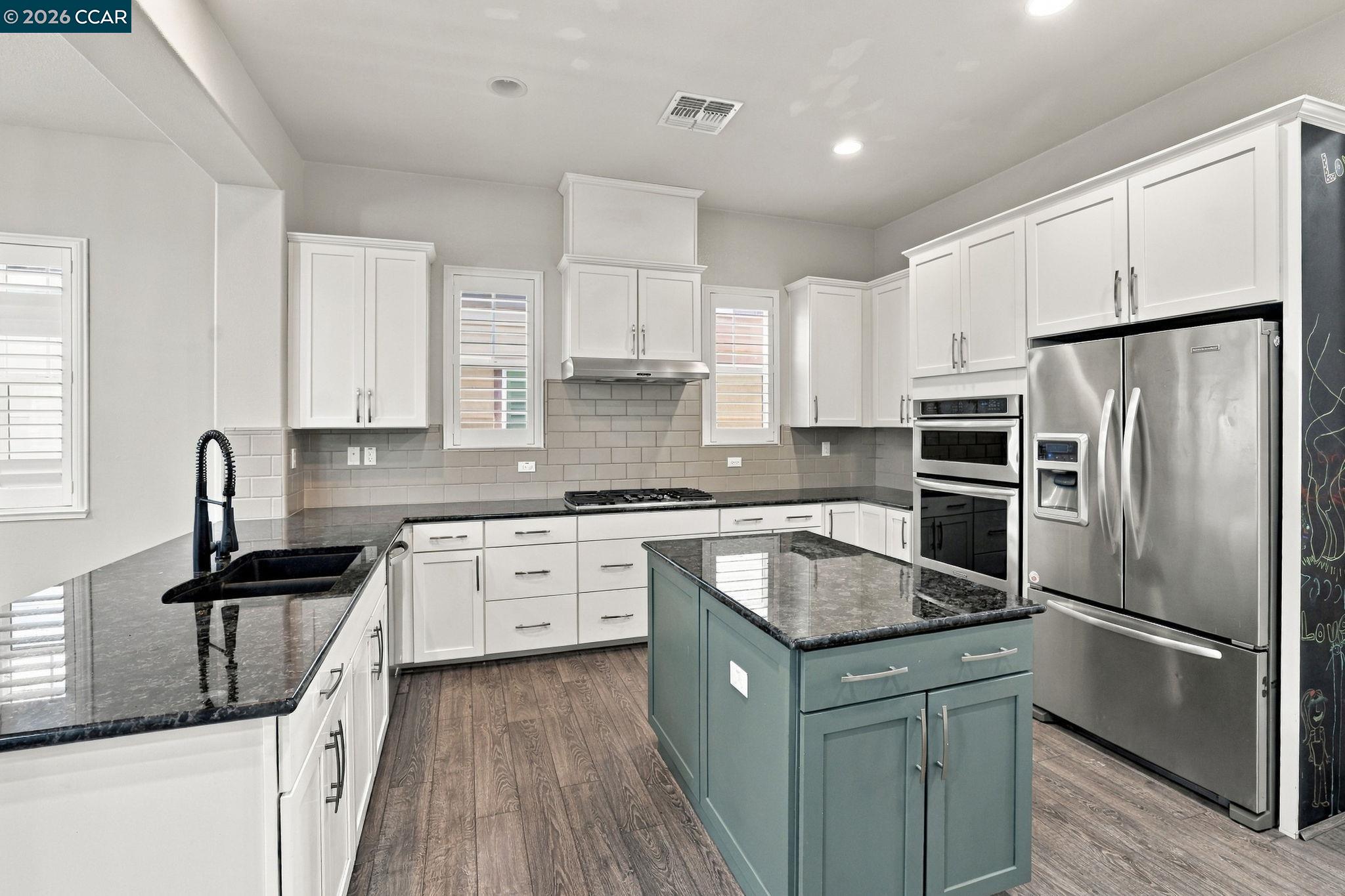 Modern kitchen with a blue-green island, dark stone counters, white cabinets, and stainless-steel appliances.