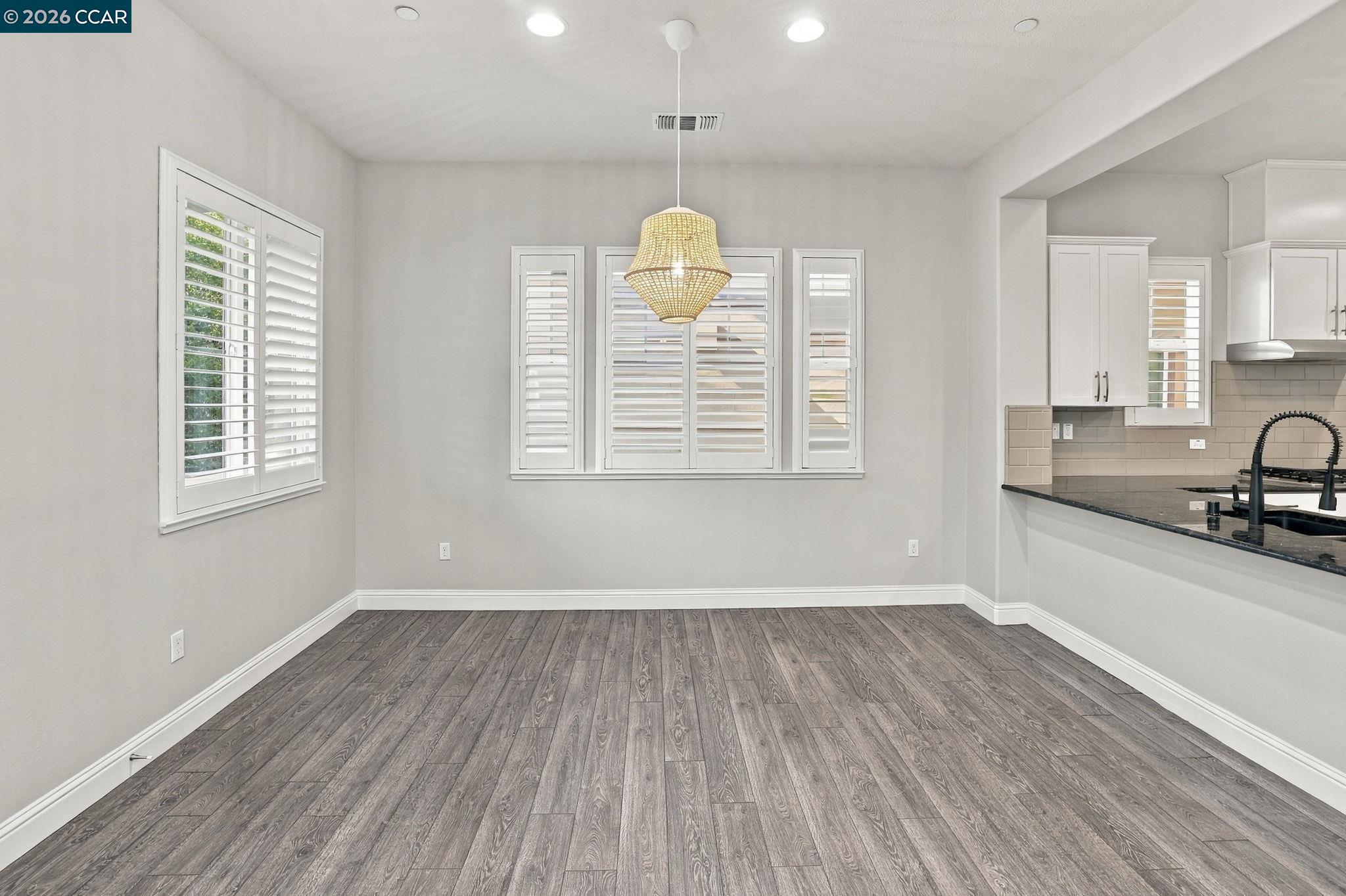 Empty dining area with plantation shutters, a woven pendant light, and an open view into the kitchen.