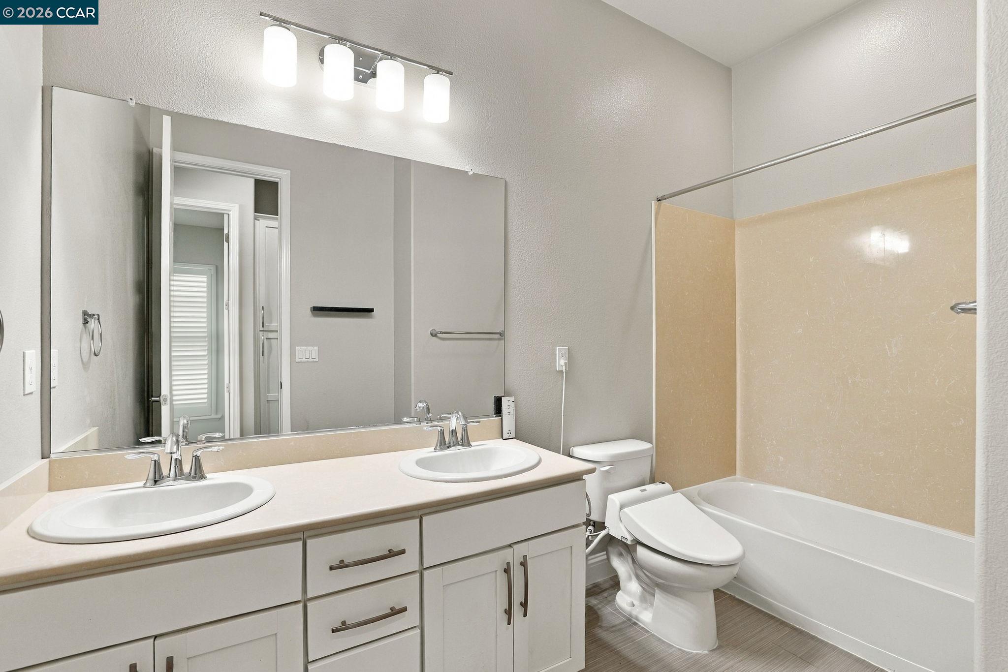 Bathroom with a double-sink vanity, large mirror, and bathtub with beige surround.