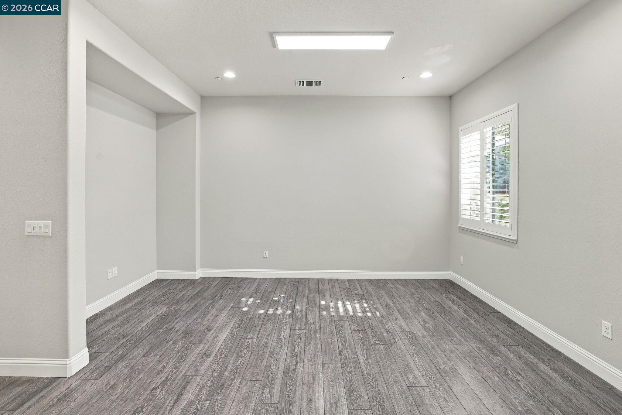 Unfurnished room with gray plank flooring, a recessed alcove, and plantation shutters.