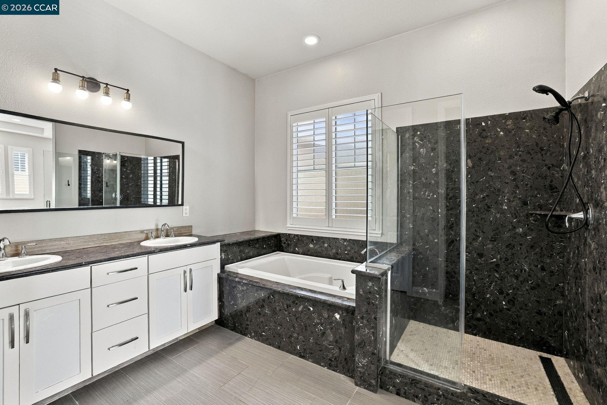 Bathroom with dual-sink vanity, soaking tub, and glass-enclosed shower with dark stone tile.