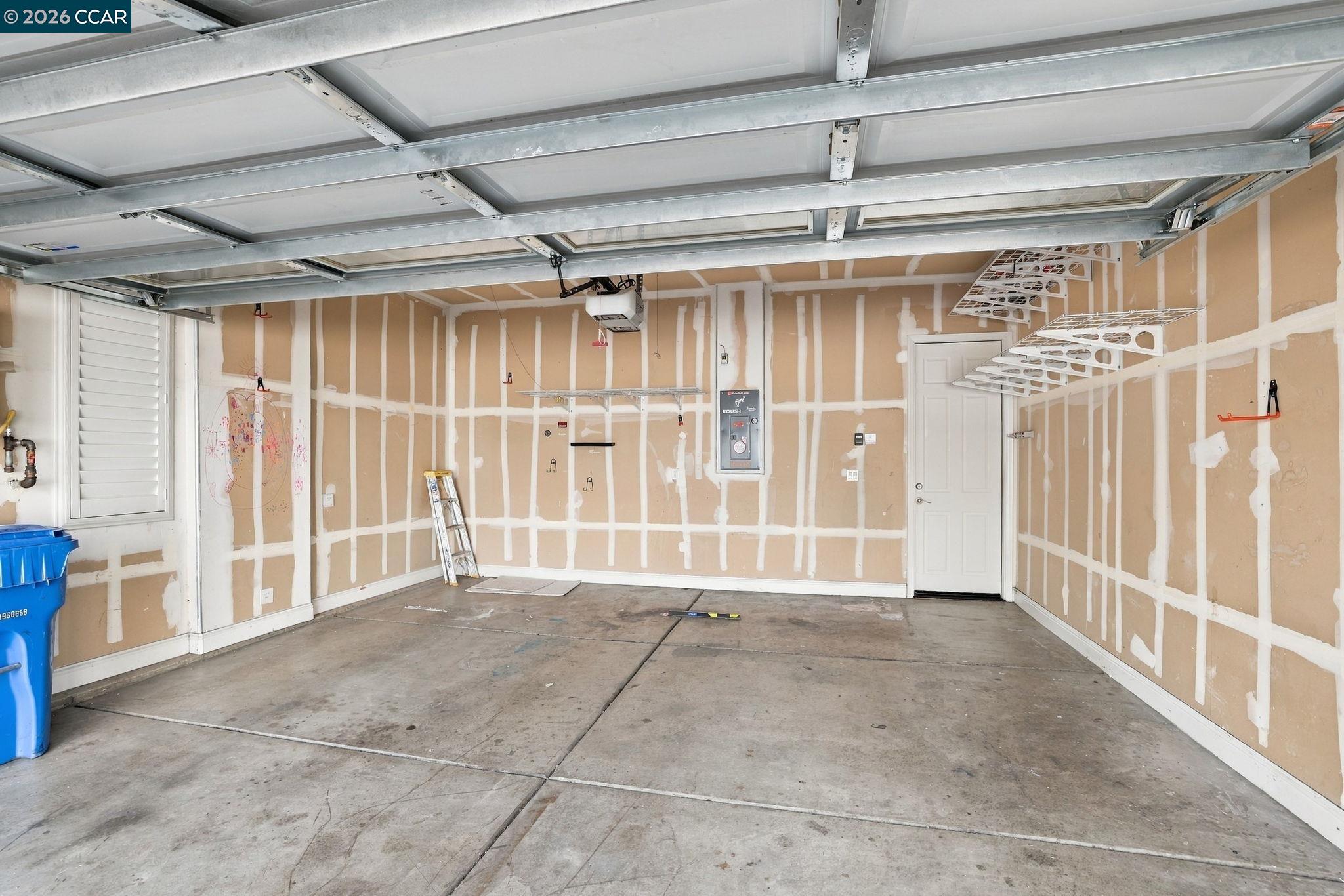 Unfinished garage with taped drywall, concrete floor, and open overhead door.