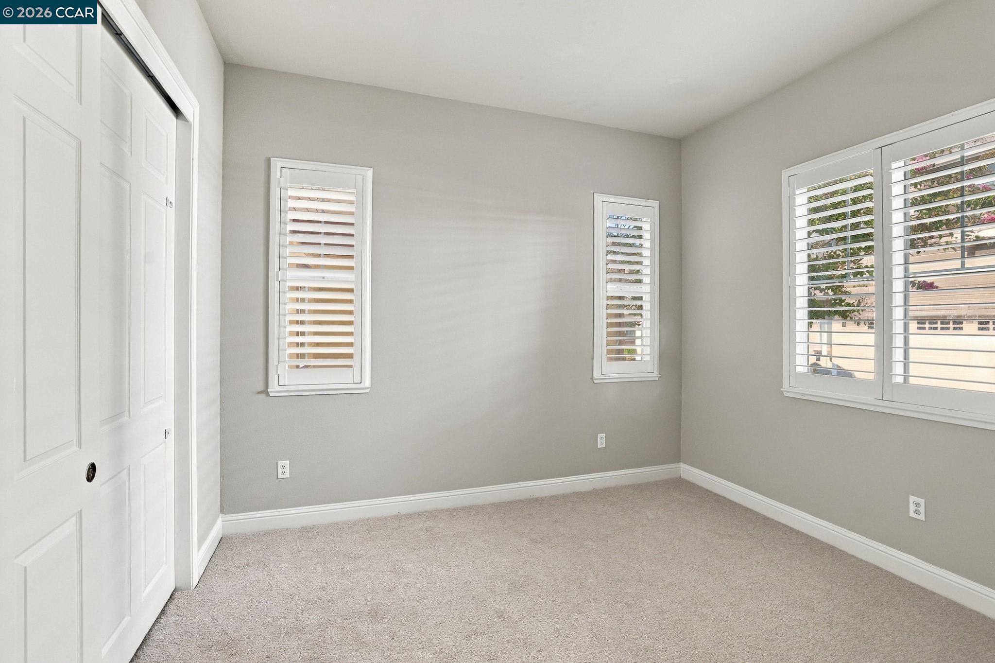Empty bedroom with beige carpet and white plantation shutters.