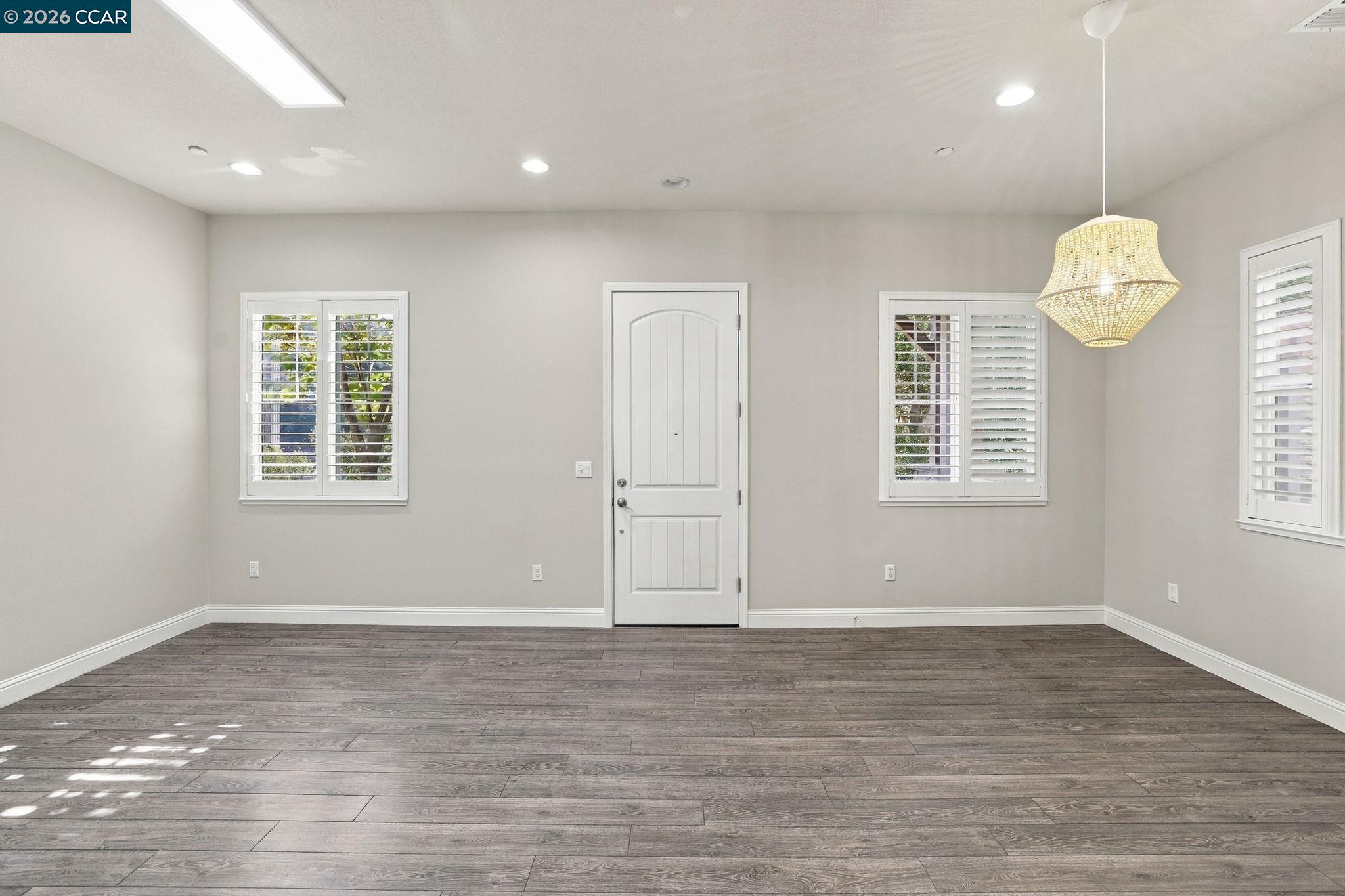 Empty interior room with gray plank flooring, shuttered windows, and a woven pendant light.