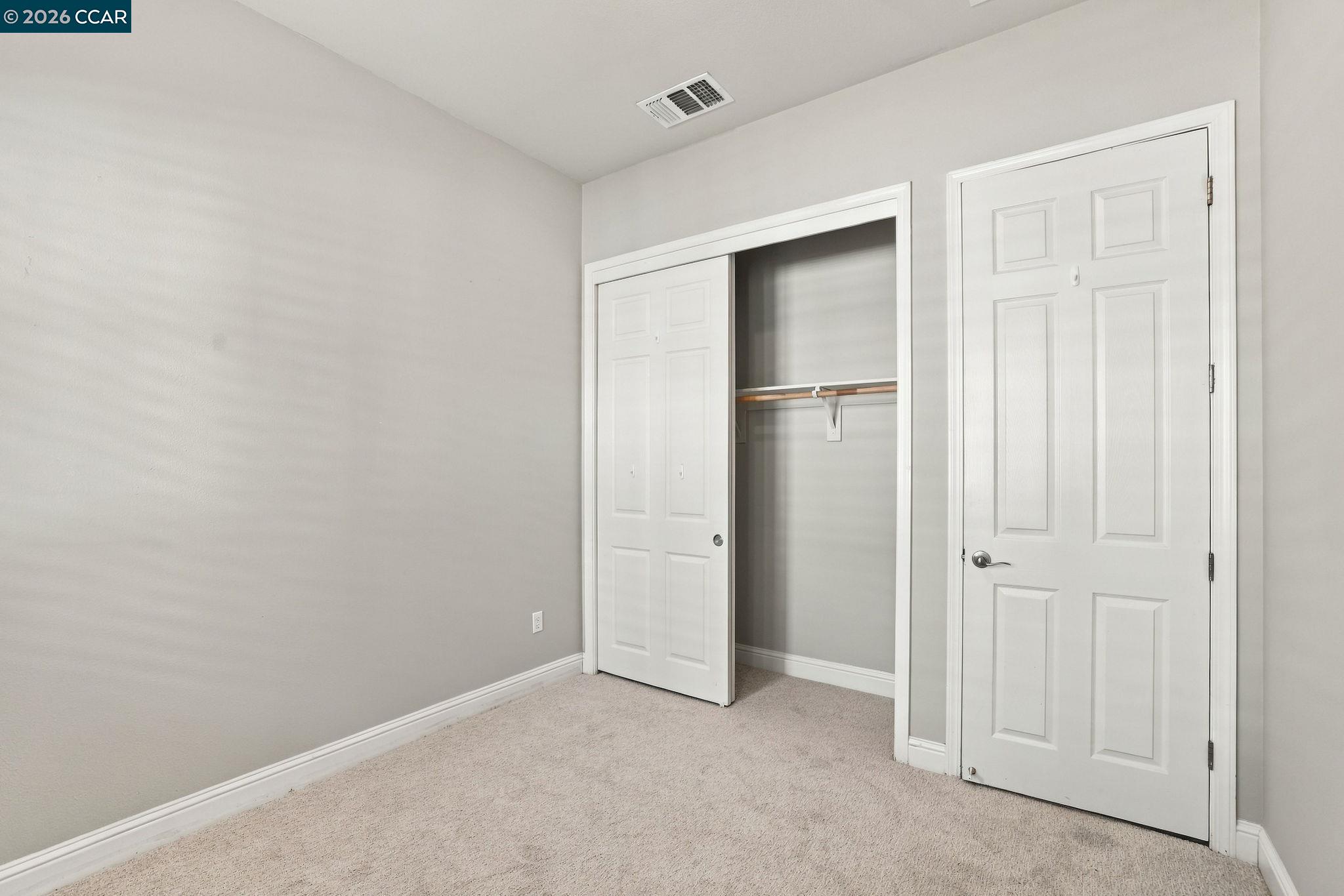 Empty carpeted bedroom with a partly open closet and white paneled door.