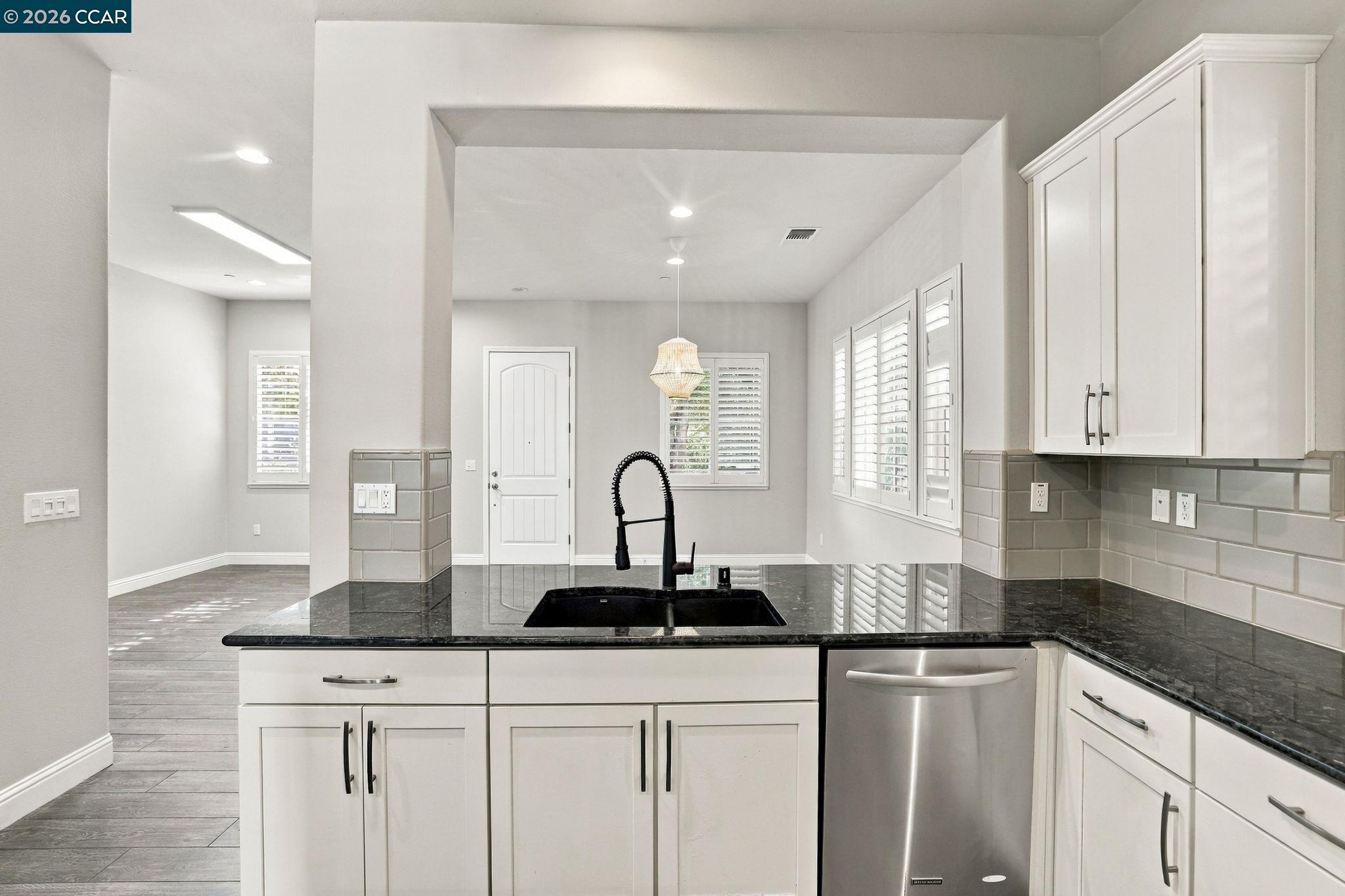 Bright kitchen with black granite counters, white cabinets, gray tile backsplash, and a stainless steel dishwasher.