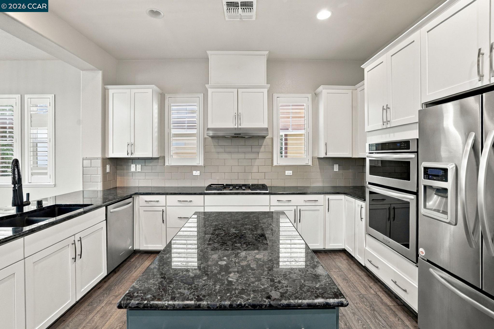 Bright kitchen with a large dark stone island, white cabinets, and stainless-steel appliances.