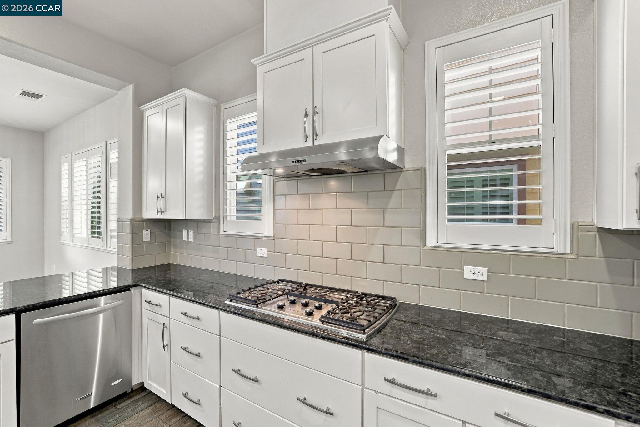 Kitchen with white cabinets, dark stone counters, gas cooktop, and plantation shutters.