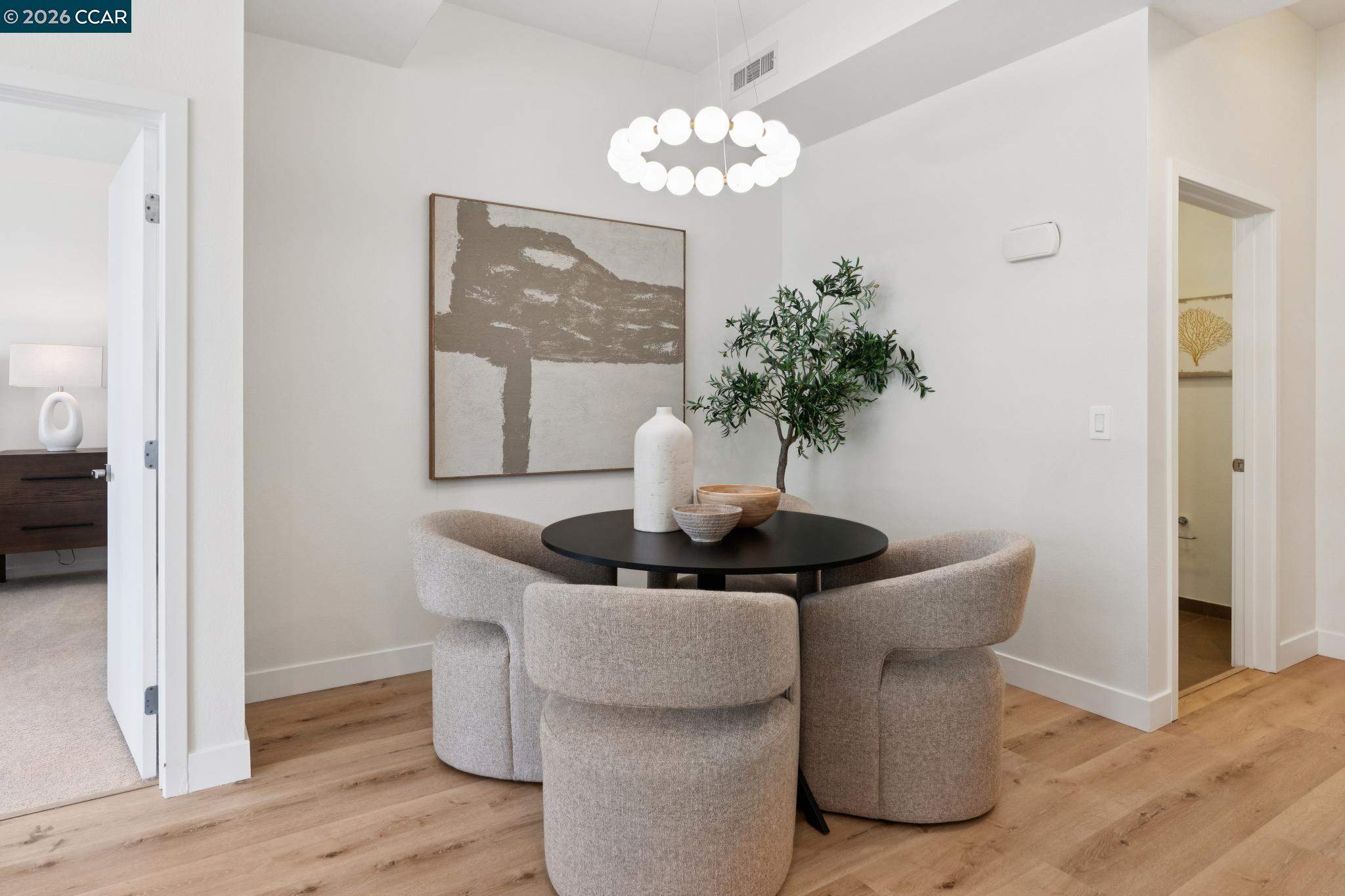 Staged dining area with a round black table, upholstered chairs, and a sculptural ring pendant light.