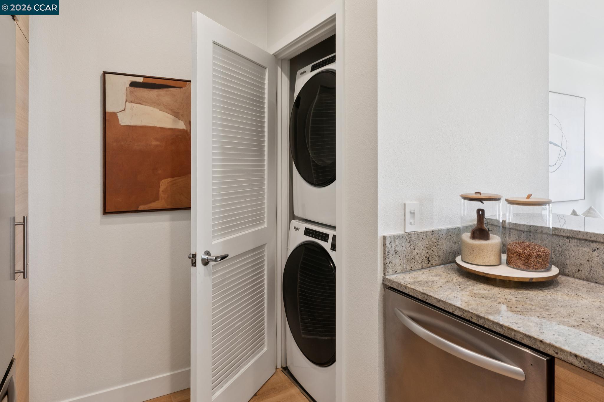 Laundry closet with stacked washer and dryer beside a granite kitchen counter.