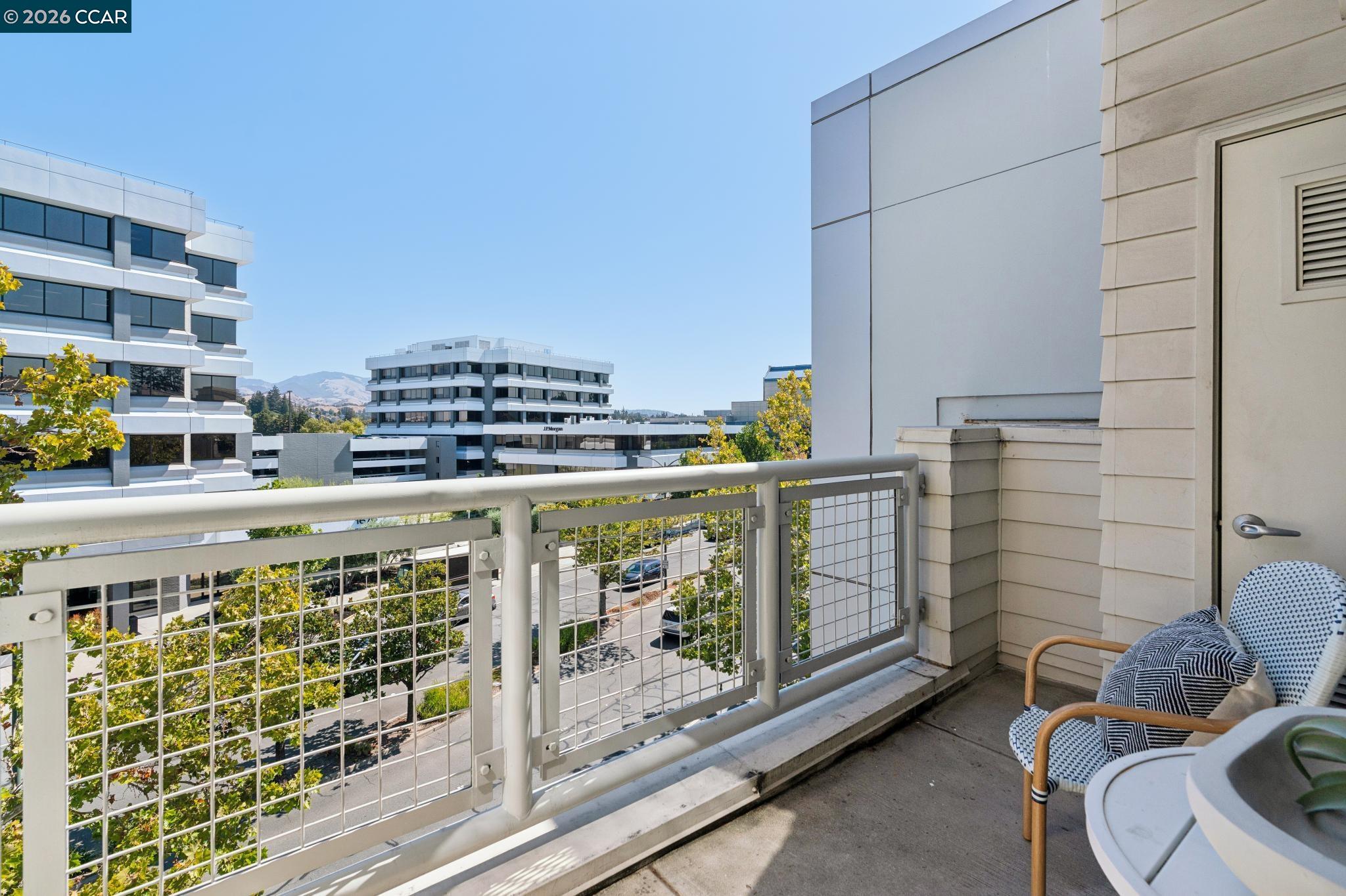 Furnished apartment balcony overlooking nearby office buildings and tree-lined streets.