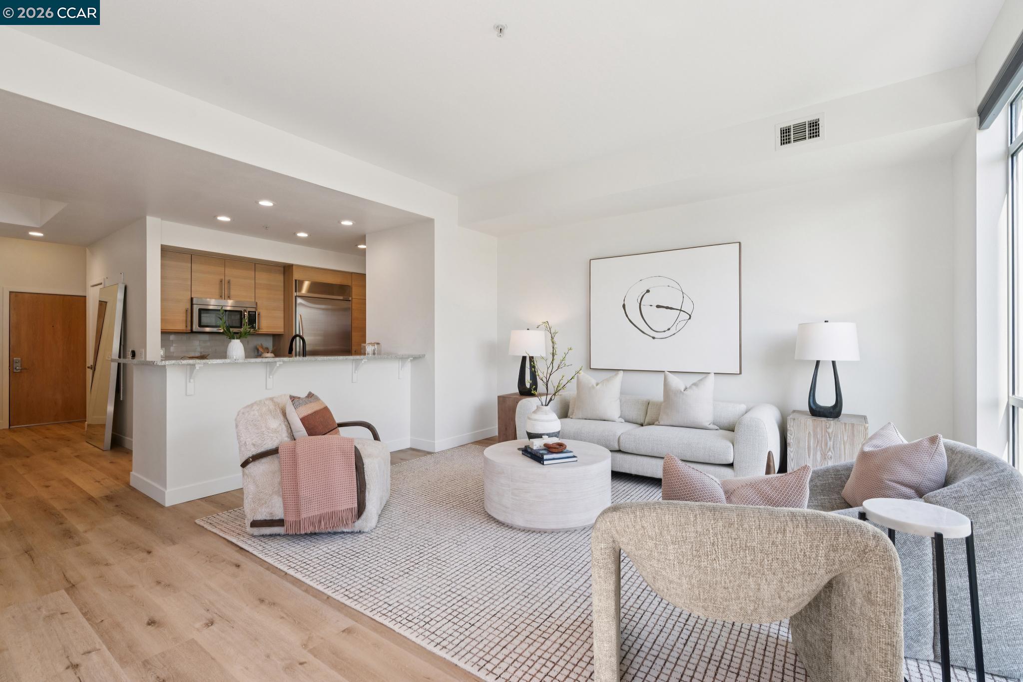 Staged condo living room with a pale sofa, abstract wall art, and open kitchen with warm wood cabinets.