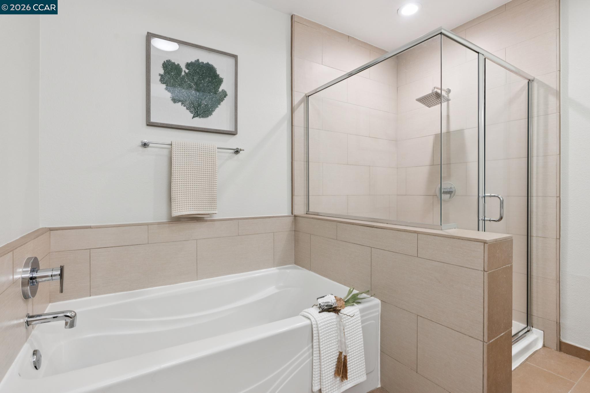 Bathroom with a white soaking tub and glass-enclosed shower, beige tile, and chrome fixtures.