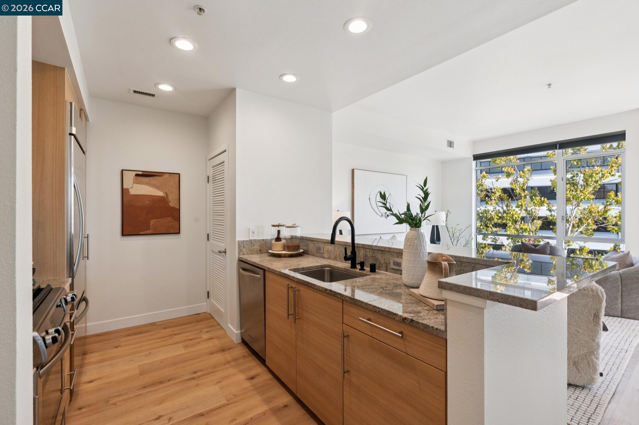 Bright condo kitchen with wood cabinetry, granite counters, and a peninsula sink beside large windows.