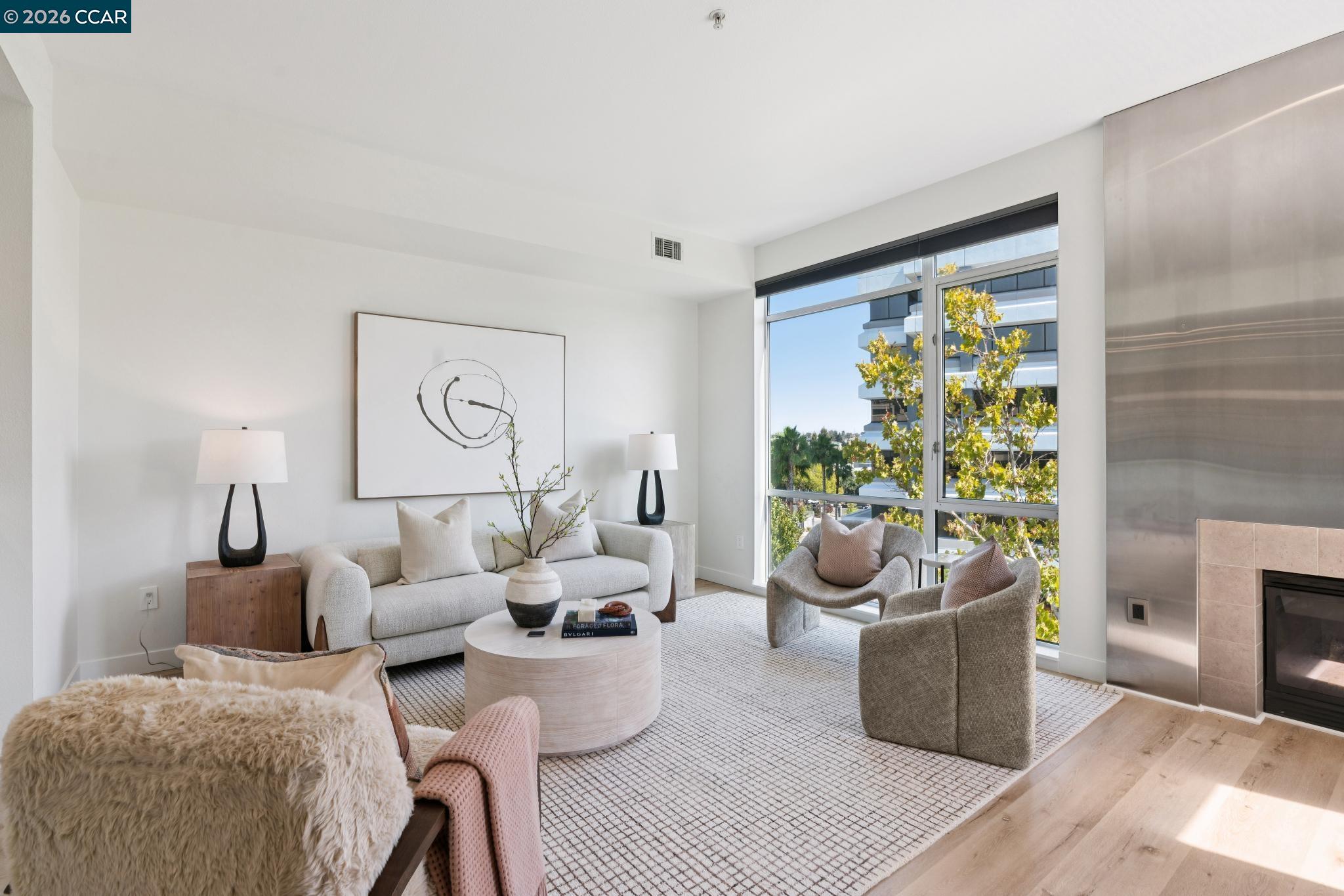 Staged condo living room with floor-to-ceiling windows, sculptural armchairs, and a fireplace.