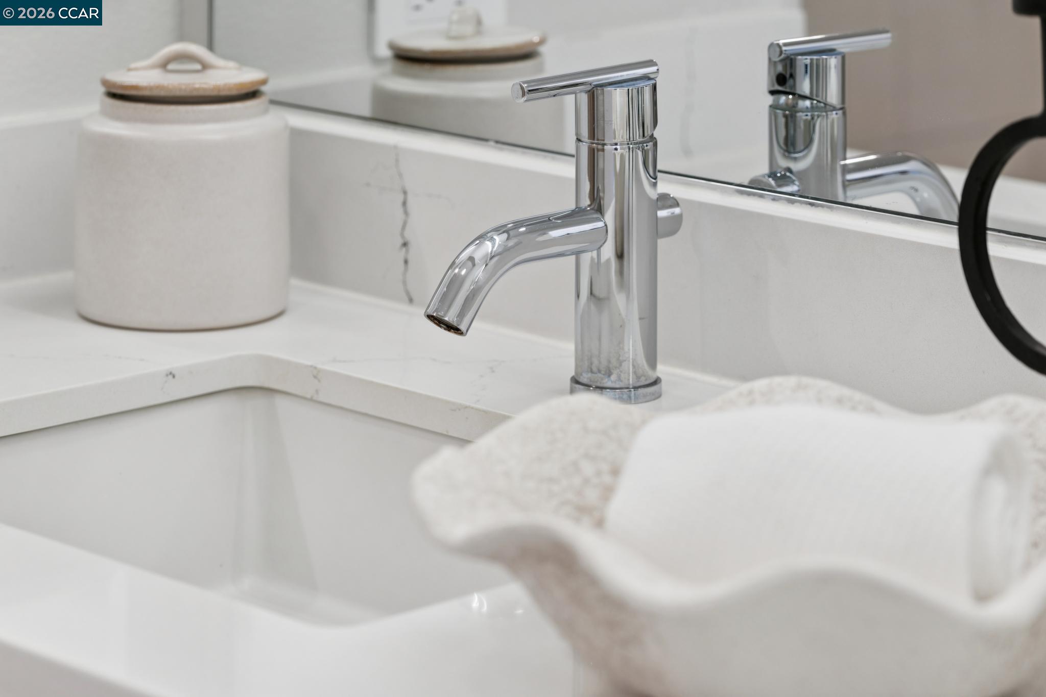 Bathroom vanity with a chrome faucet, white veined countertop, mirror, and folded towel.