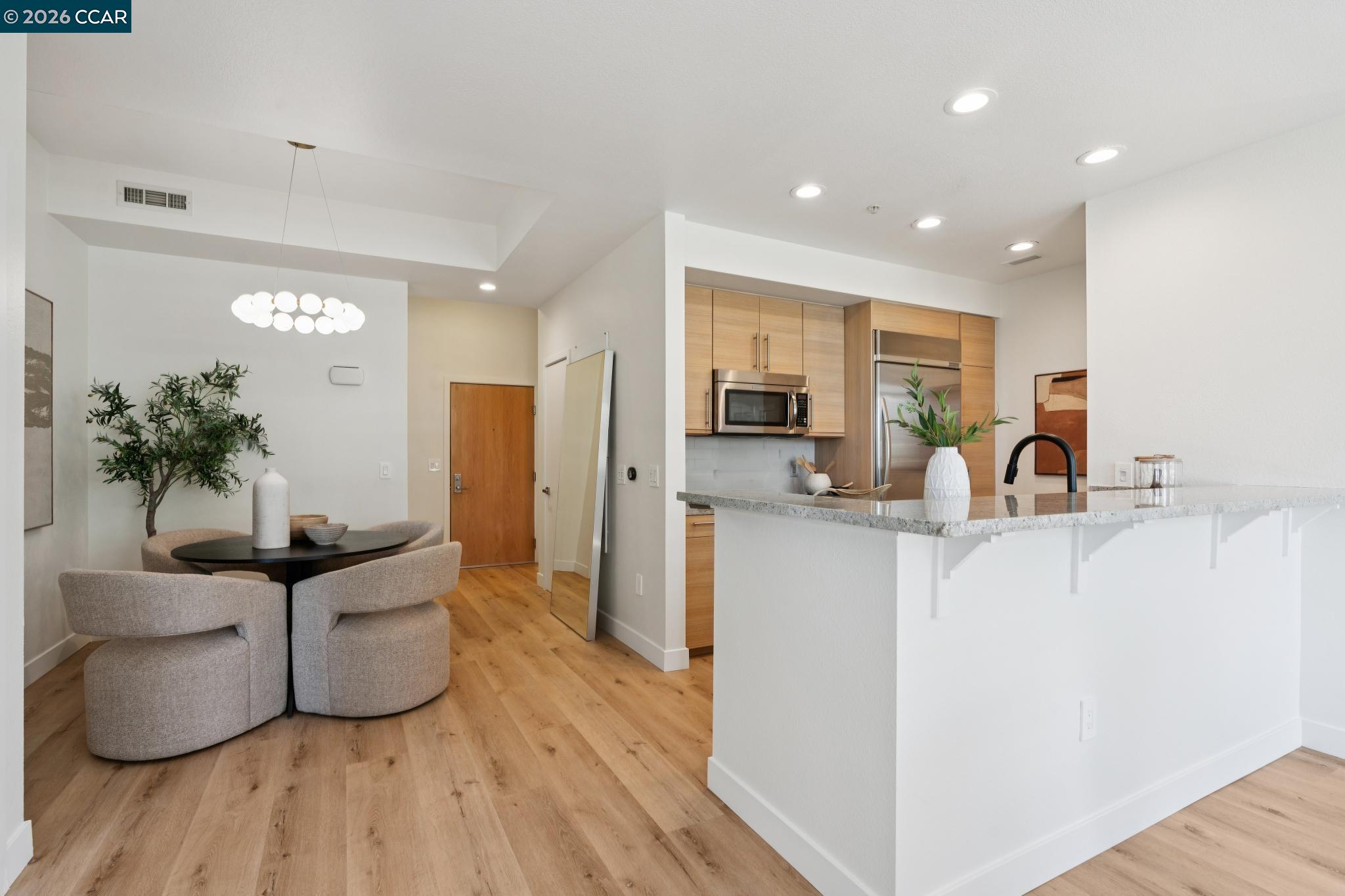 Open kitchen and dining area with a large island, light wood cabinetry, and upholstered chairs.
