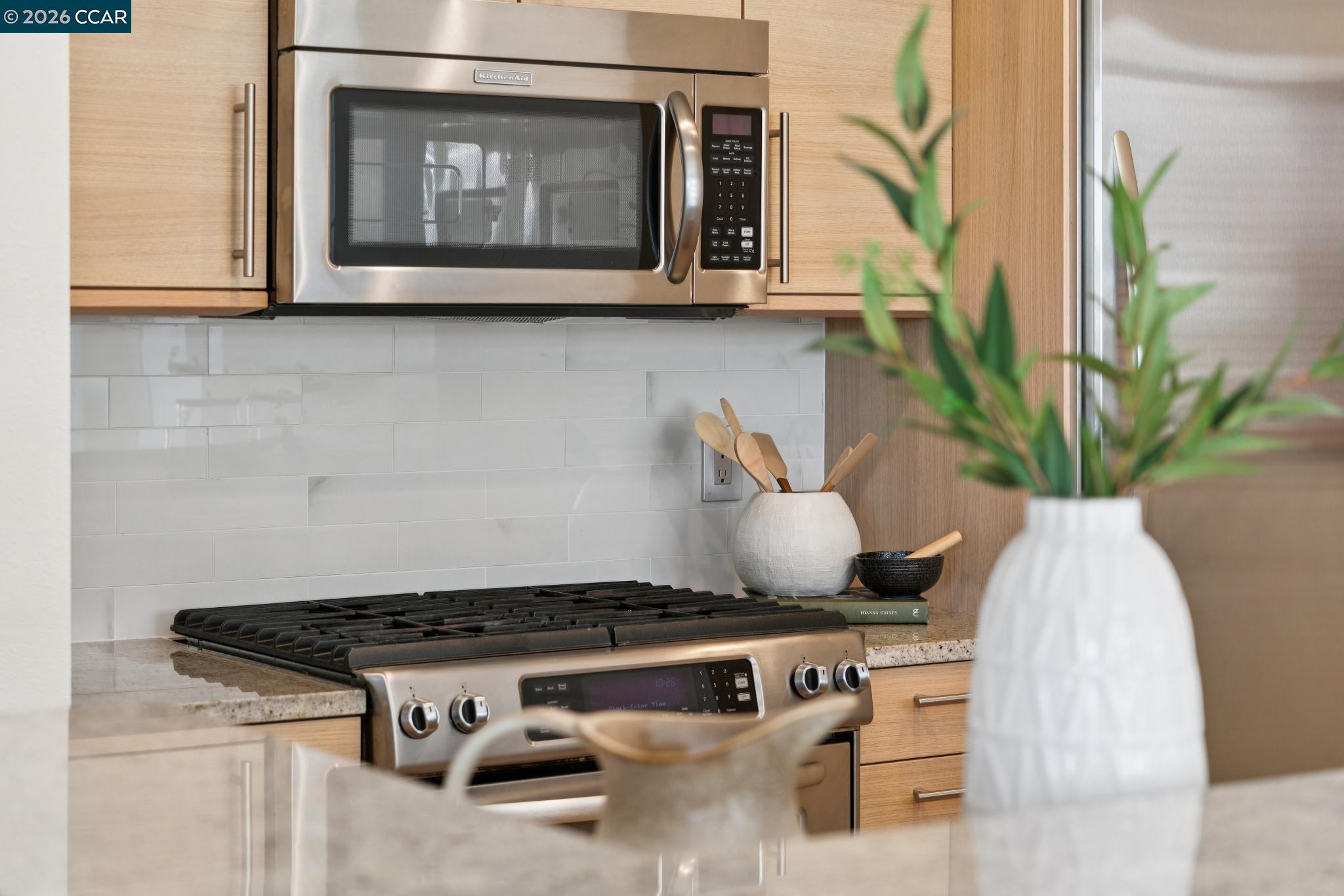Kitchen with stainless steel range and microwave, light wood cabinets, and a white tile backsplash.