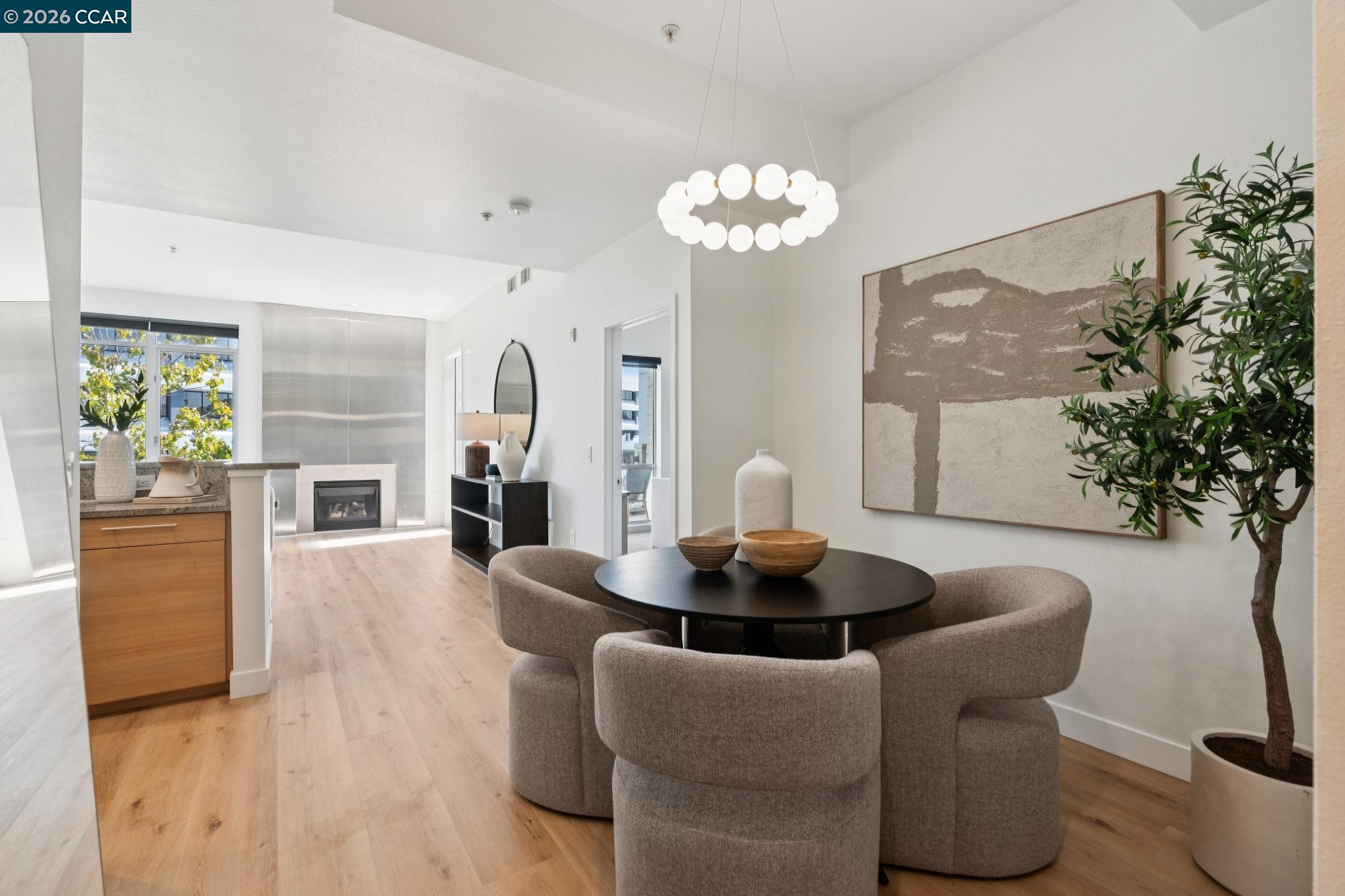 Open-plan condo dining area with a round black table, upholstered chairs, kitchen, and fireplace.