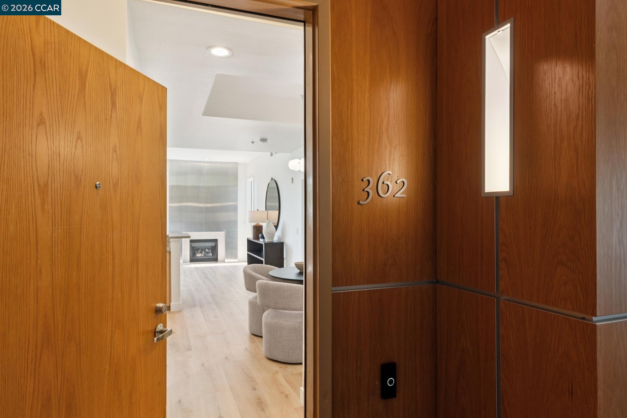 Open wood entry door marked 362 reveals a bright living area with a fireplace and rounded chairs.