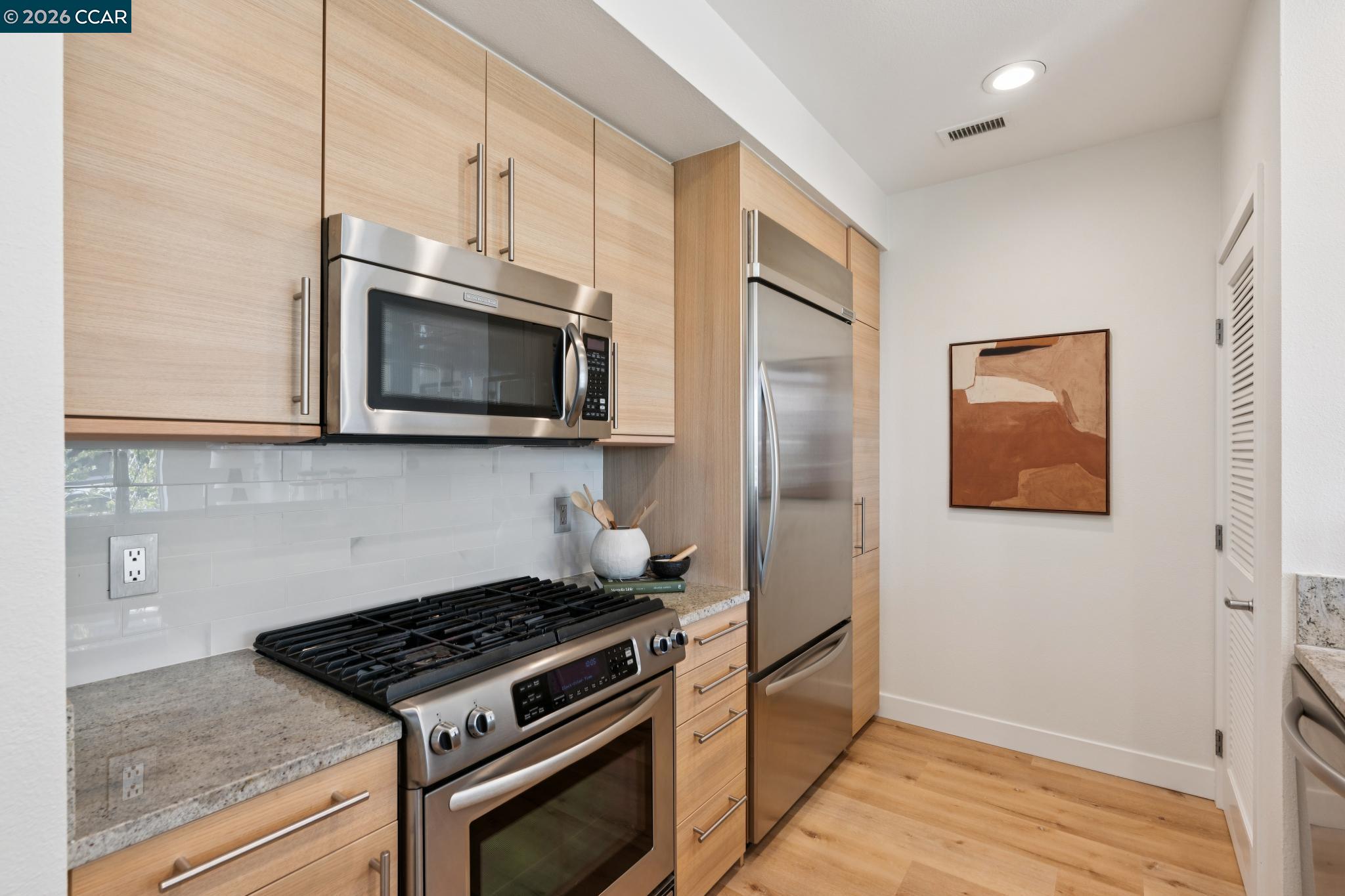 Modern kitchen with light wood cabinets, stainless steel appliances, and a gas range.