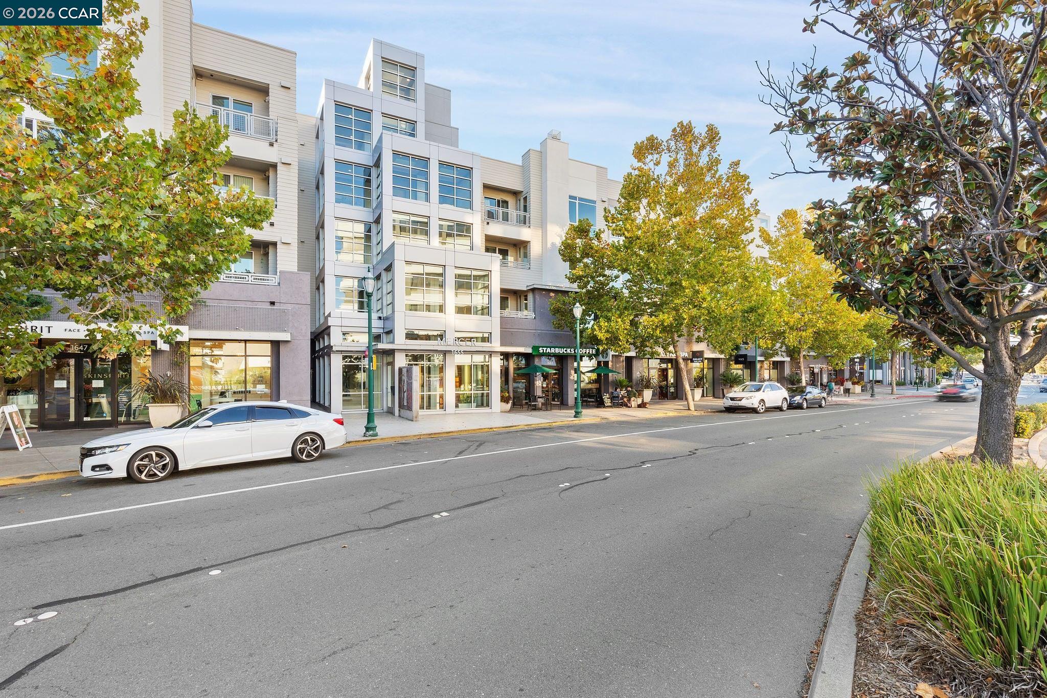 Modern mixed-use building with balconies, ground-floor shops, and autumn trees along the sidewalk.