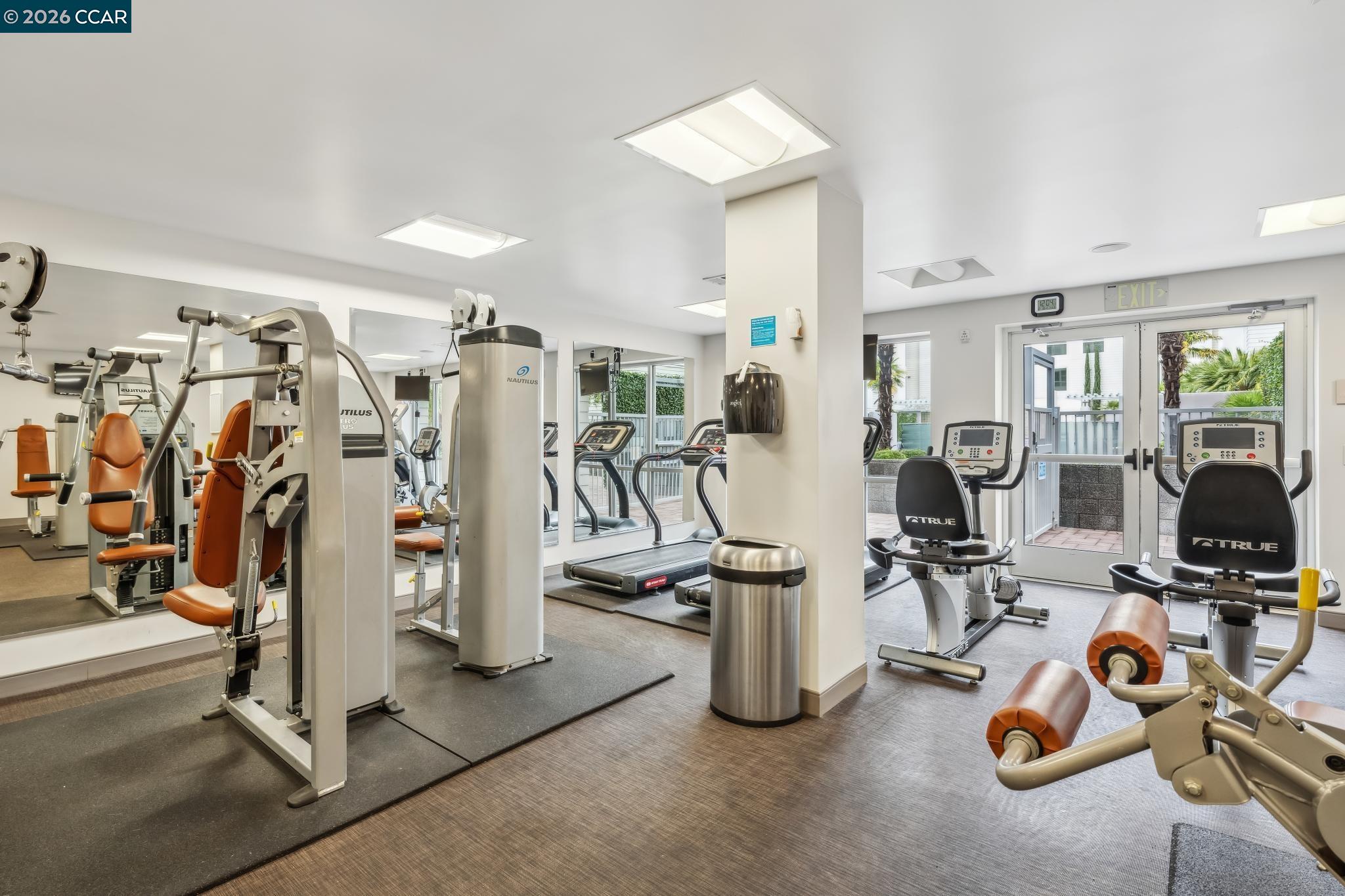 Fitness center with weight machines, treadmills, and stationary bikes beside glass doors to a patio.