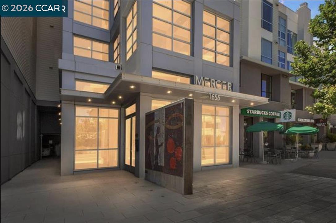 Mercer building exterior with tall glowing windows, covered entrance, and Starbucks patio.