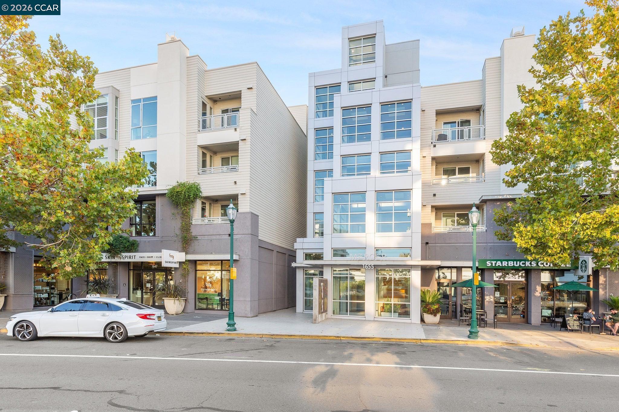 Modern multi-story condominium building with ground-floor shops and autumn street trees.