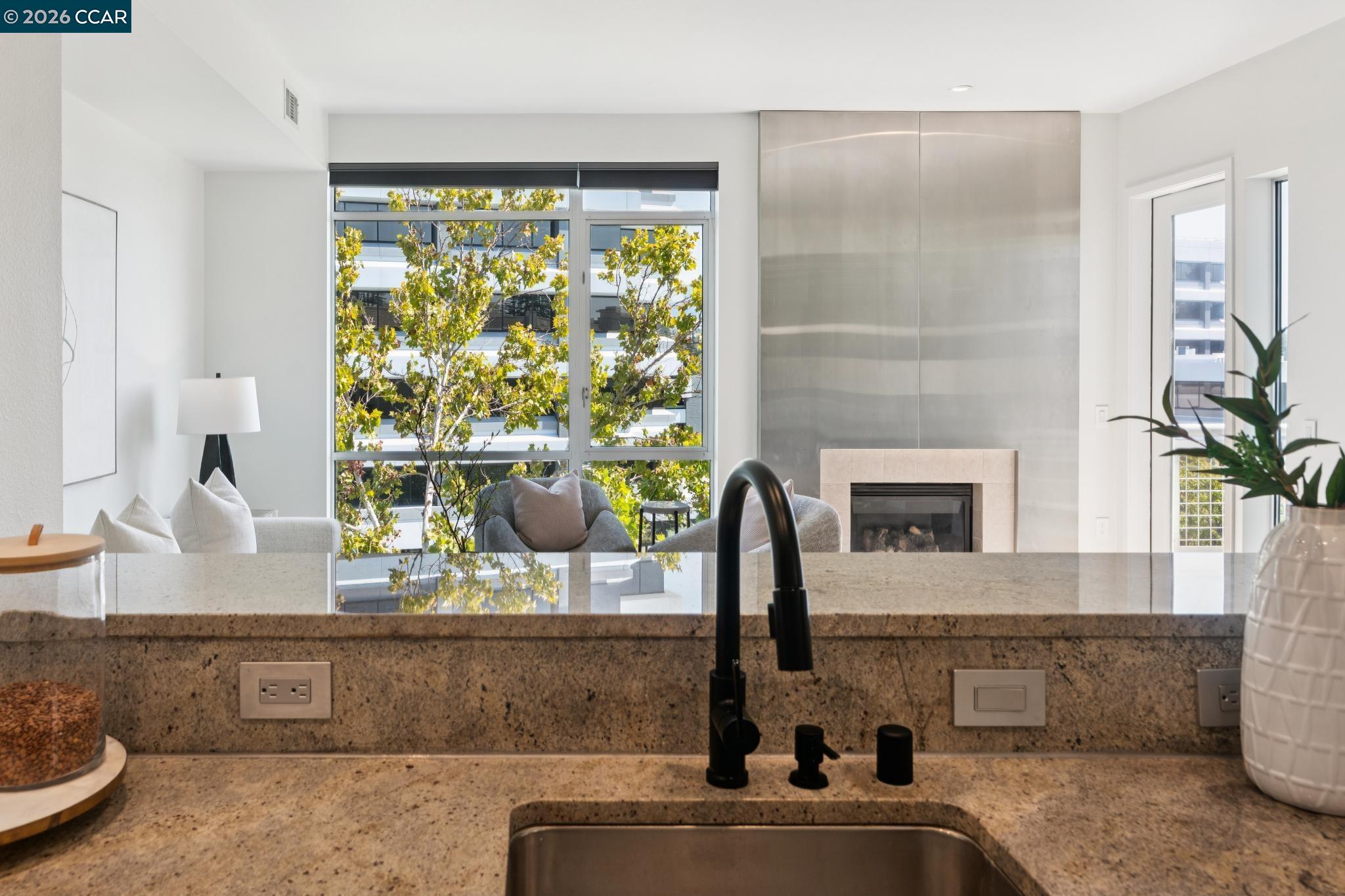 Modern kitchen with a stone counter, black faucet, and windows overlooking leafy trees.