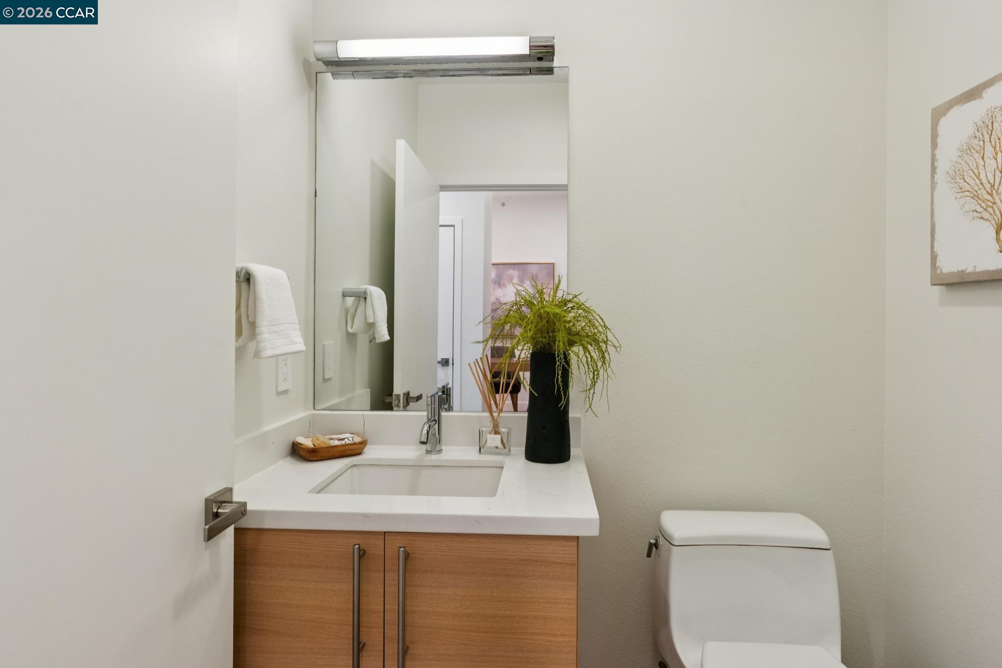 Bathroom with wood vanity, white sink, large mirror, and modern toilet.