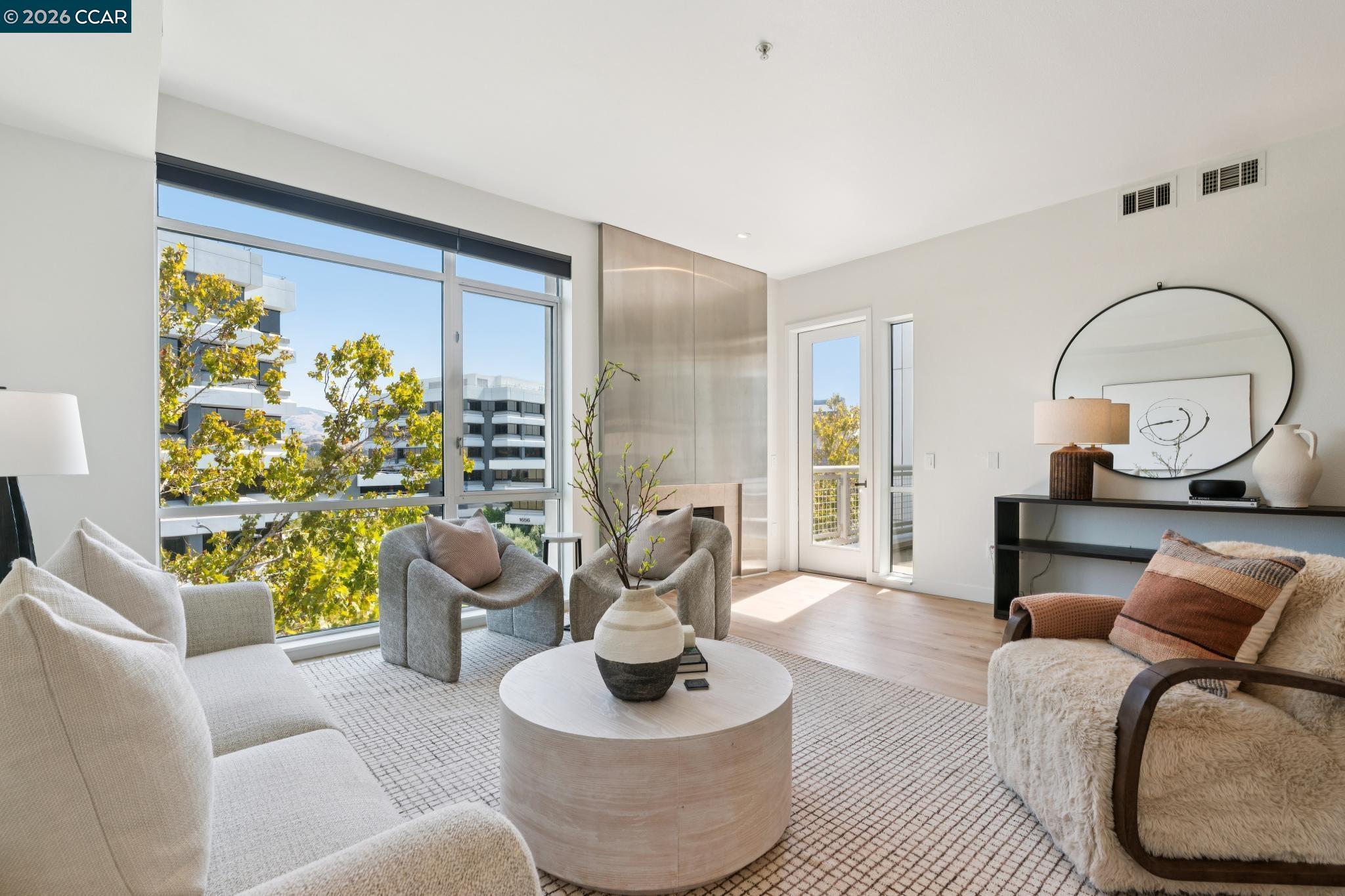 Furnished living room with floor-to-ceiling windows, sculptural chairs, and a built-in fireplace.