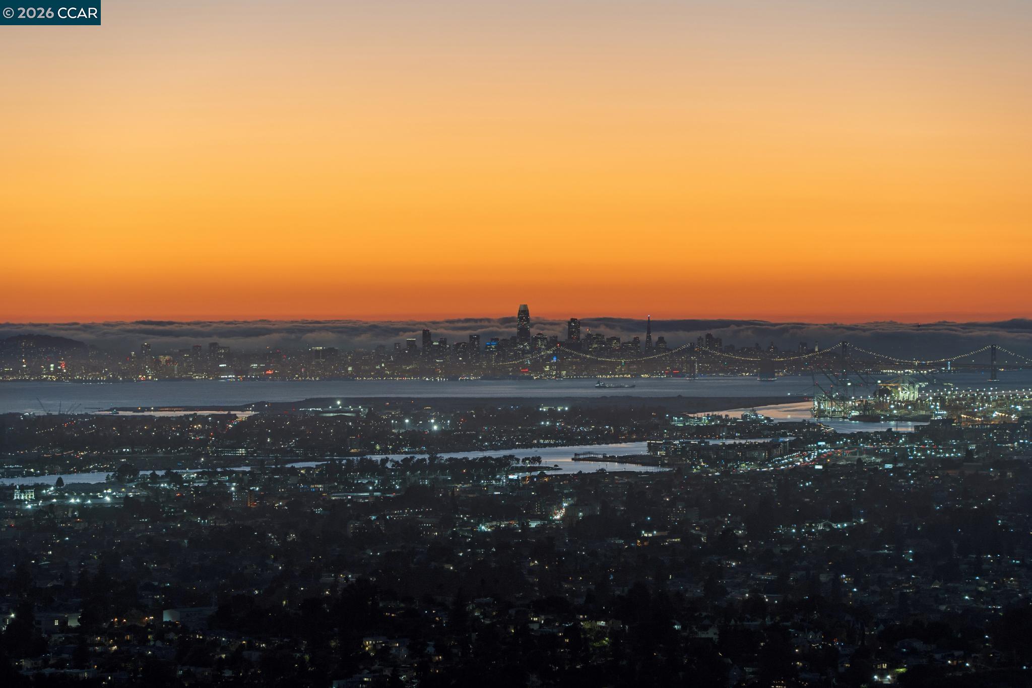 San Francisco skyline across the bay at dusk, with illuminated bridges beneath an orange sunset sky.