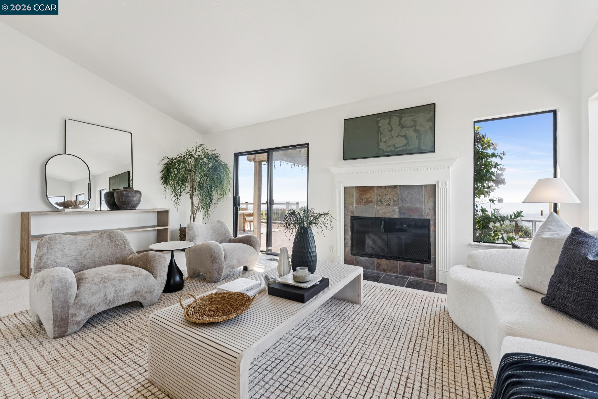 Staged living room with a stone fireplace, cream seating, and glass doors opening to a deck.