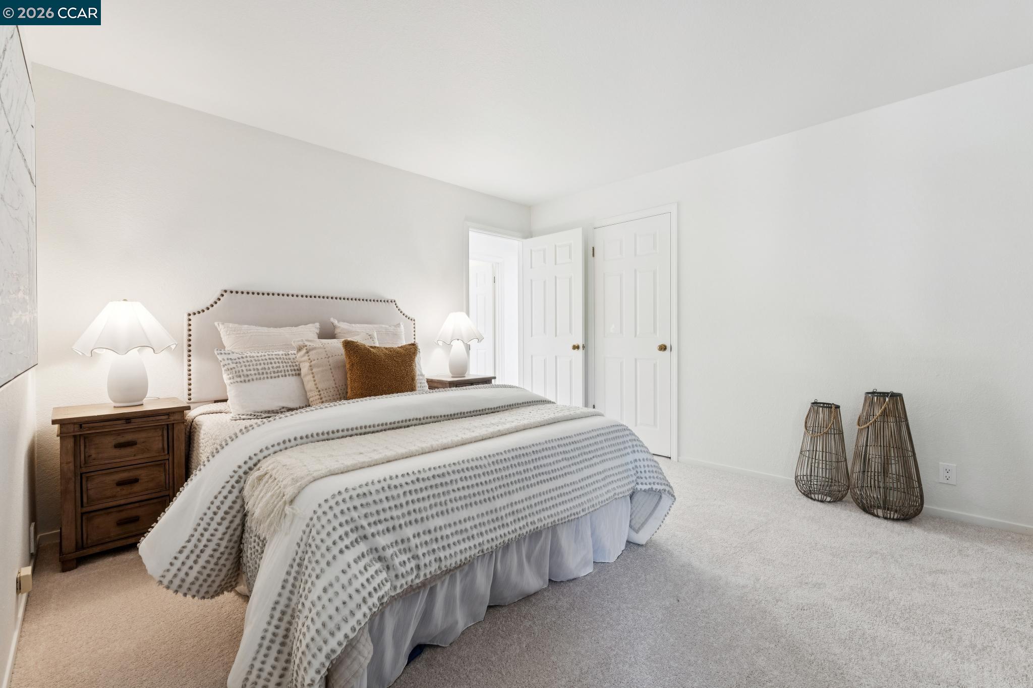 Staged bedroom with patterned white bedding, a nailhead-trim headboard, and woven floor lanterns.