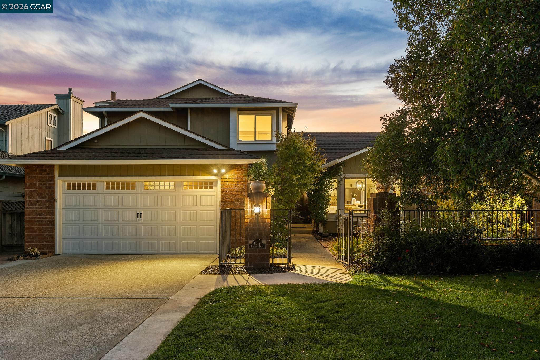 Two-story home at dusk with a double garage, brick accents, and a gated garden walkway.