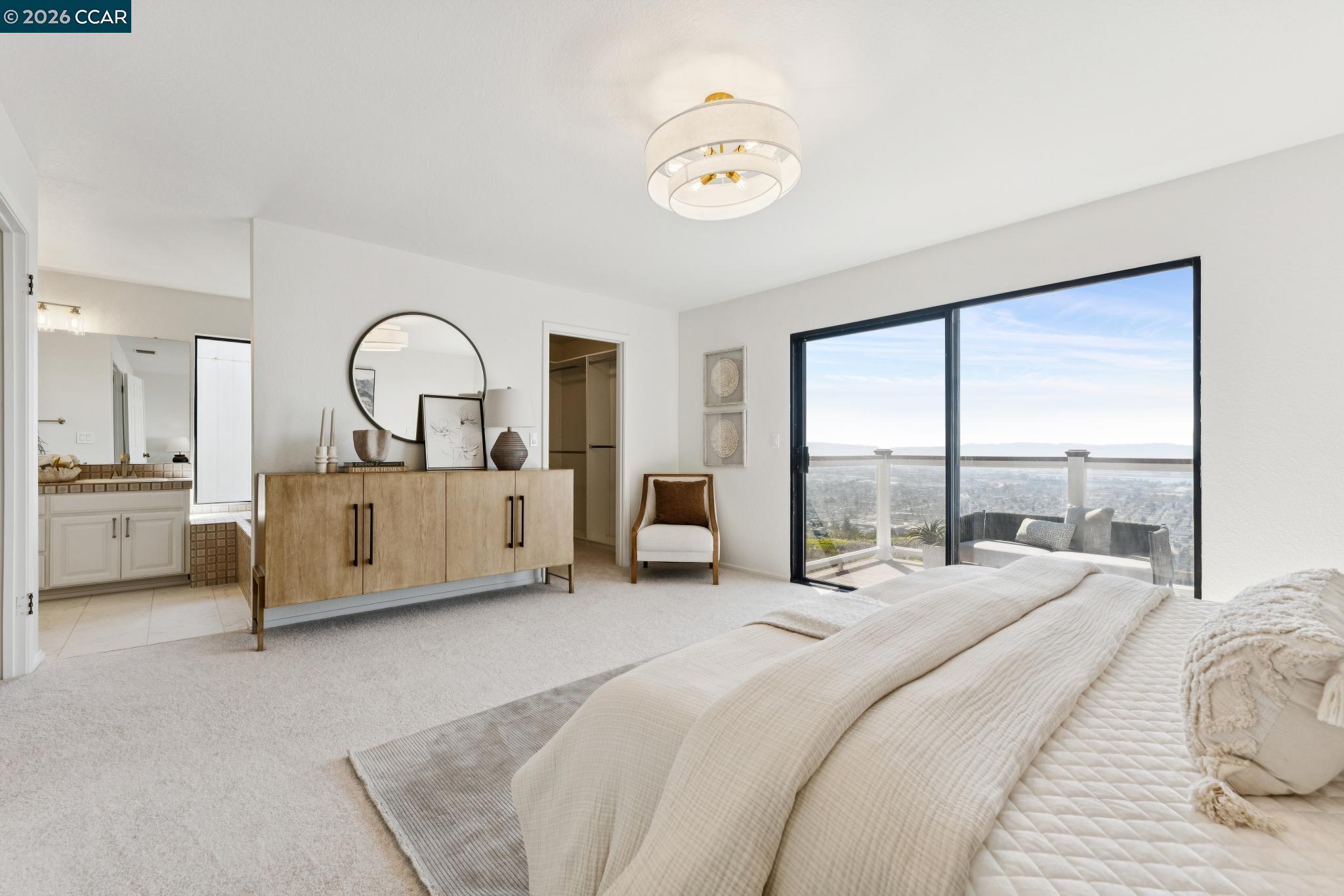 Staged primary bedroom with a large bed and sliding doors opening to a balcony with a distant city view.