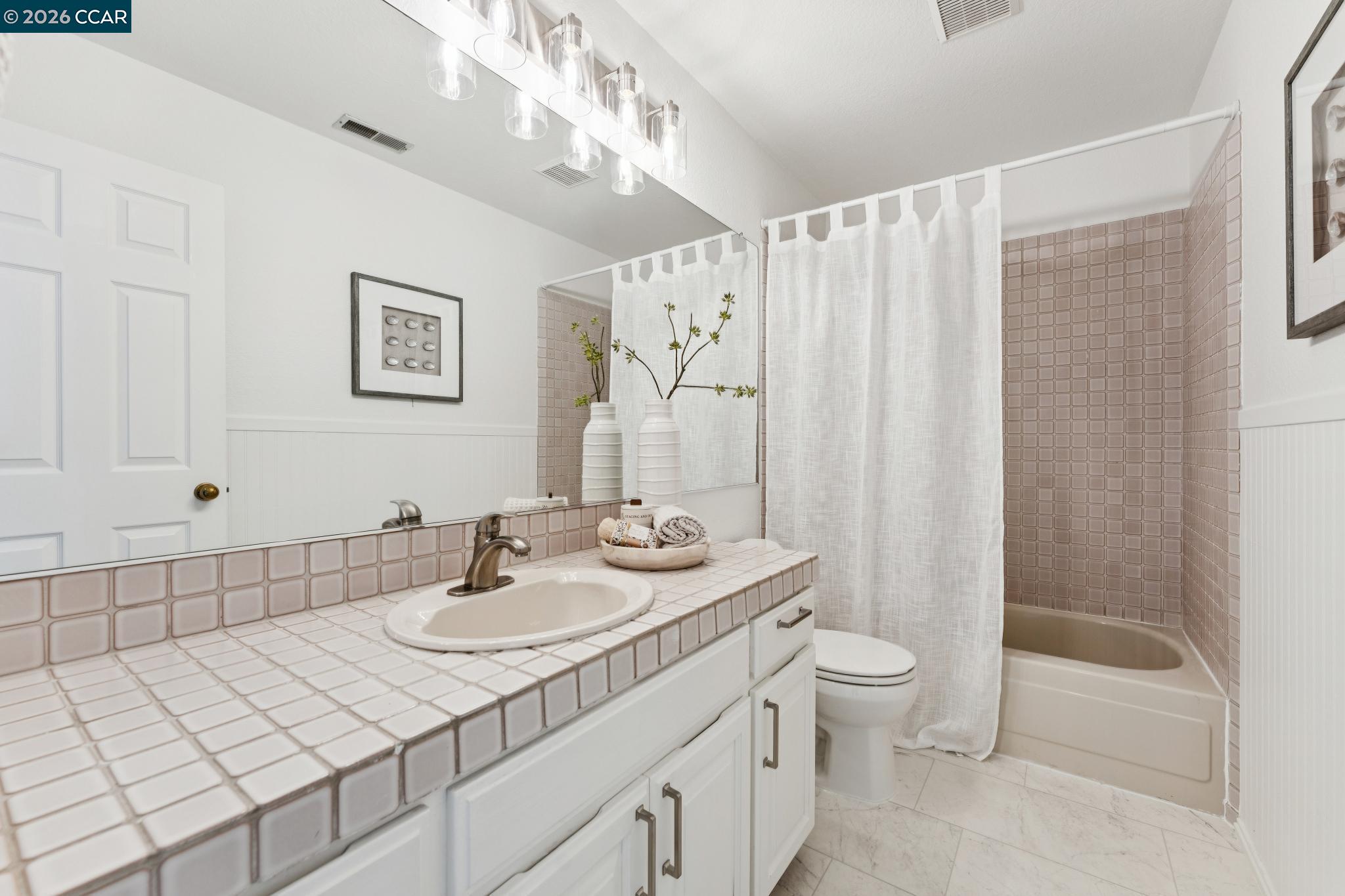 Bathroom with a pale pink tiled vanity and bathtub behind a white shower curtain.
