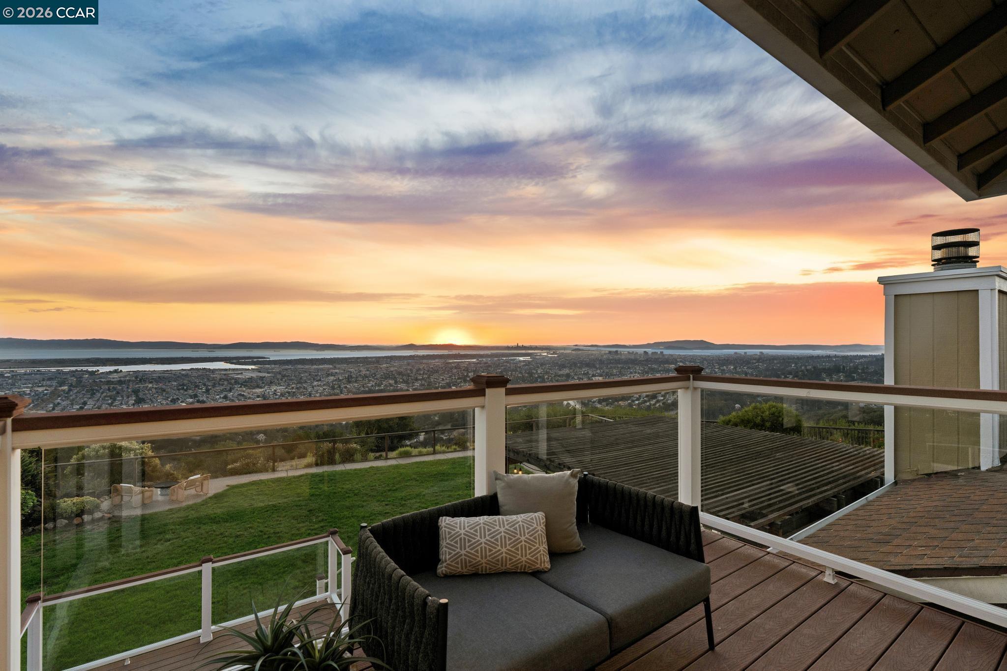 Rooftop deck with glass railings and seating overlooking the bay at sunset.