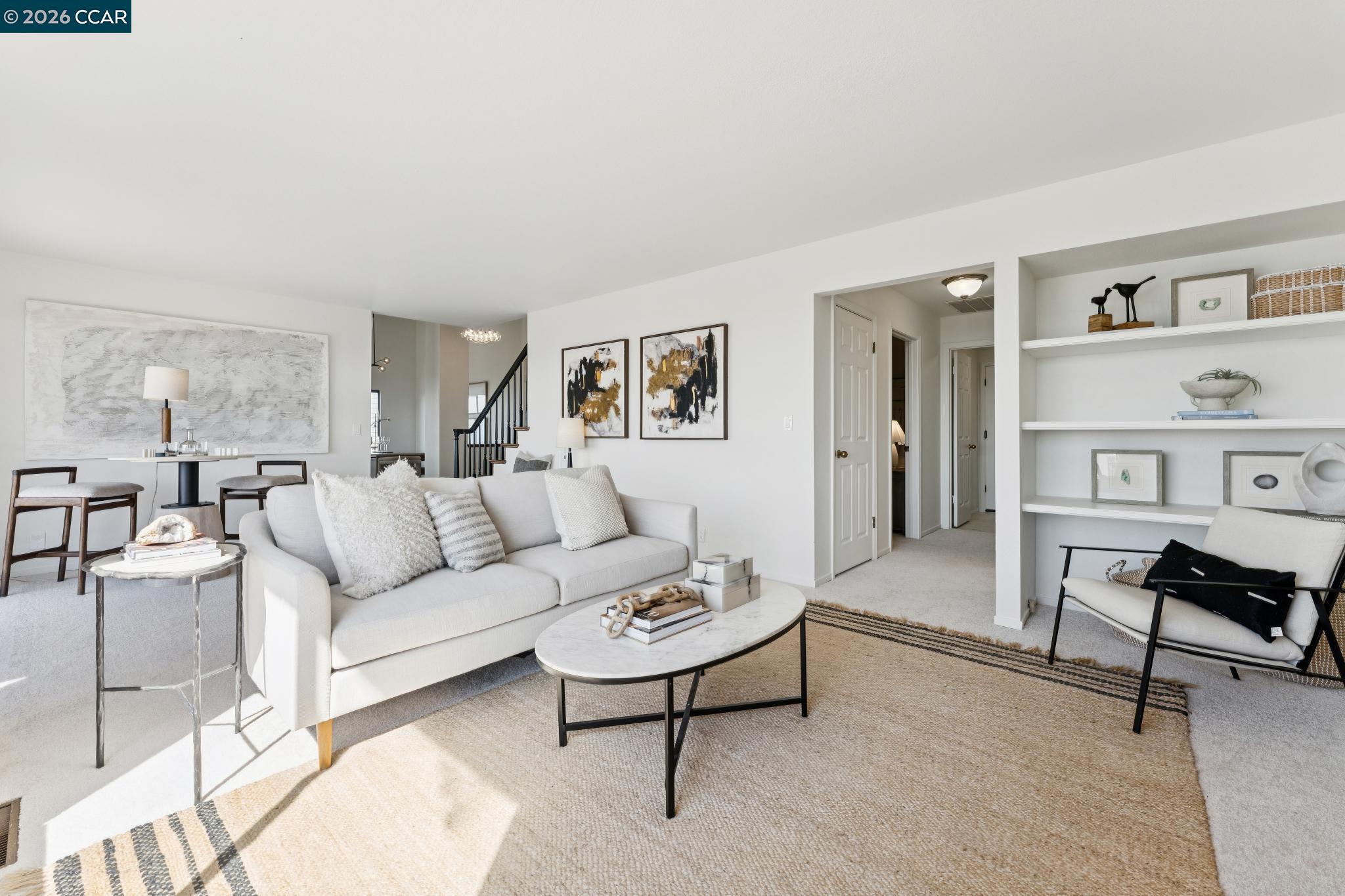 Staged living room with a white sofa, marble coffee table, woven rug, and built-in shelves.