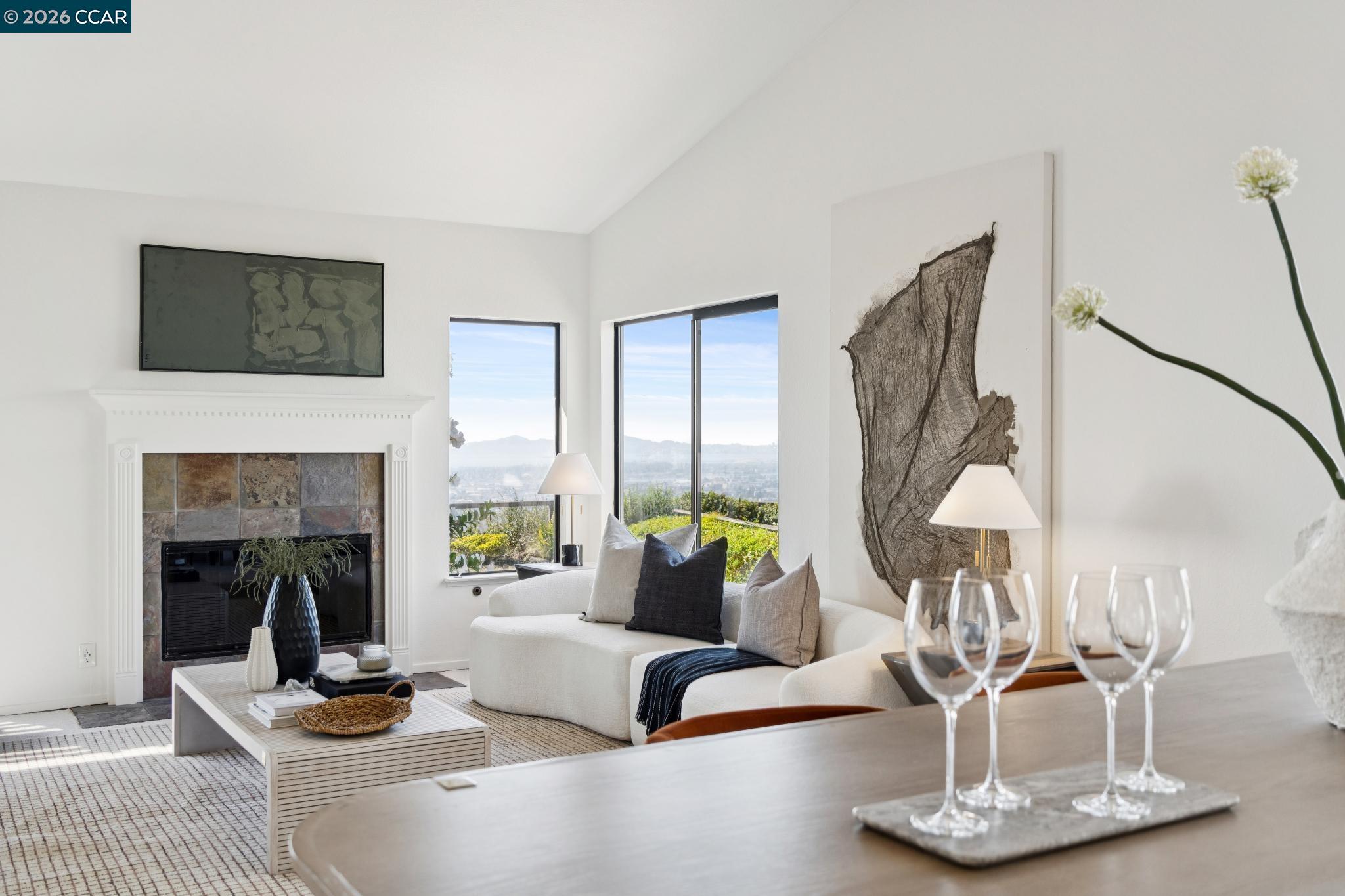Living room with a white fireplace, contemporary furnishings, and windows overlooking a distant cityscape.