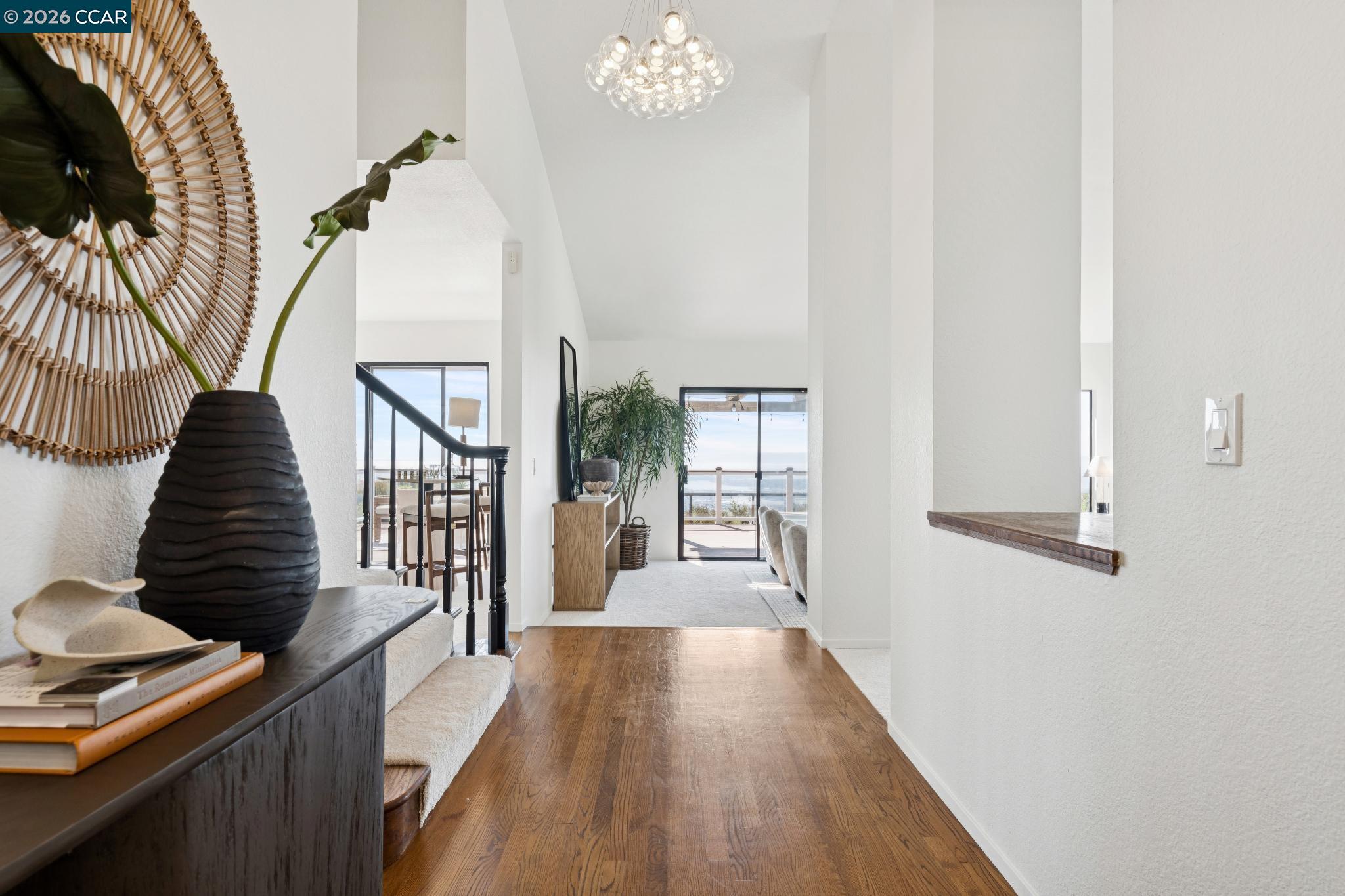 Bright entry hall with hardwood floors, staircase, and glass doors overlooking the water.