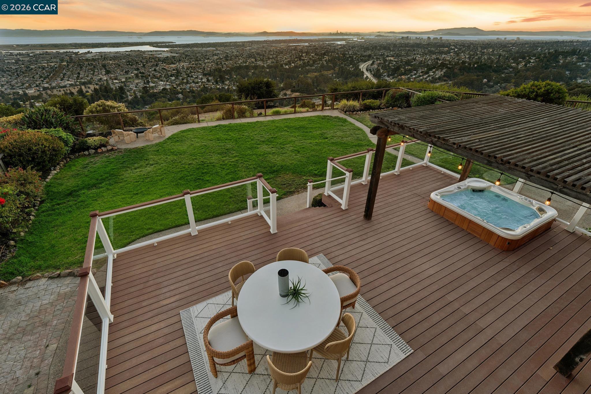 Backyard deck with a pergola and hot tub overlooking Oakland and the bay at sunset.