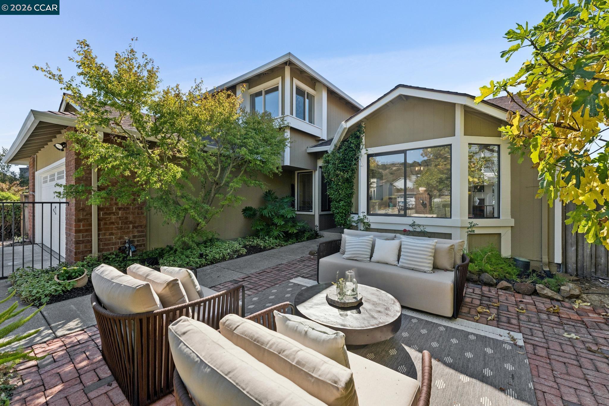 Furnished brick patio with cushioned seating and a round table outside a two-story home.